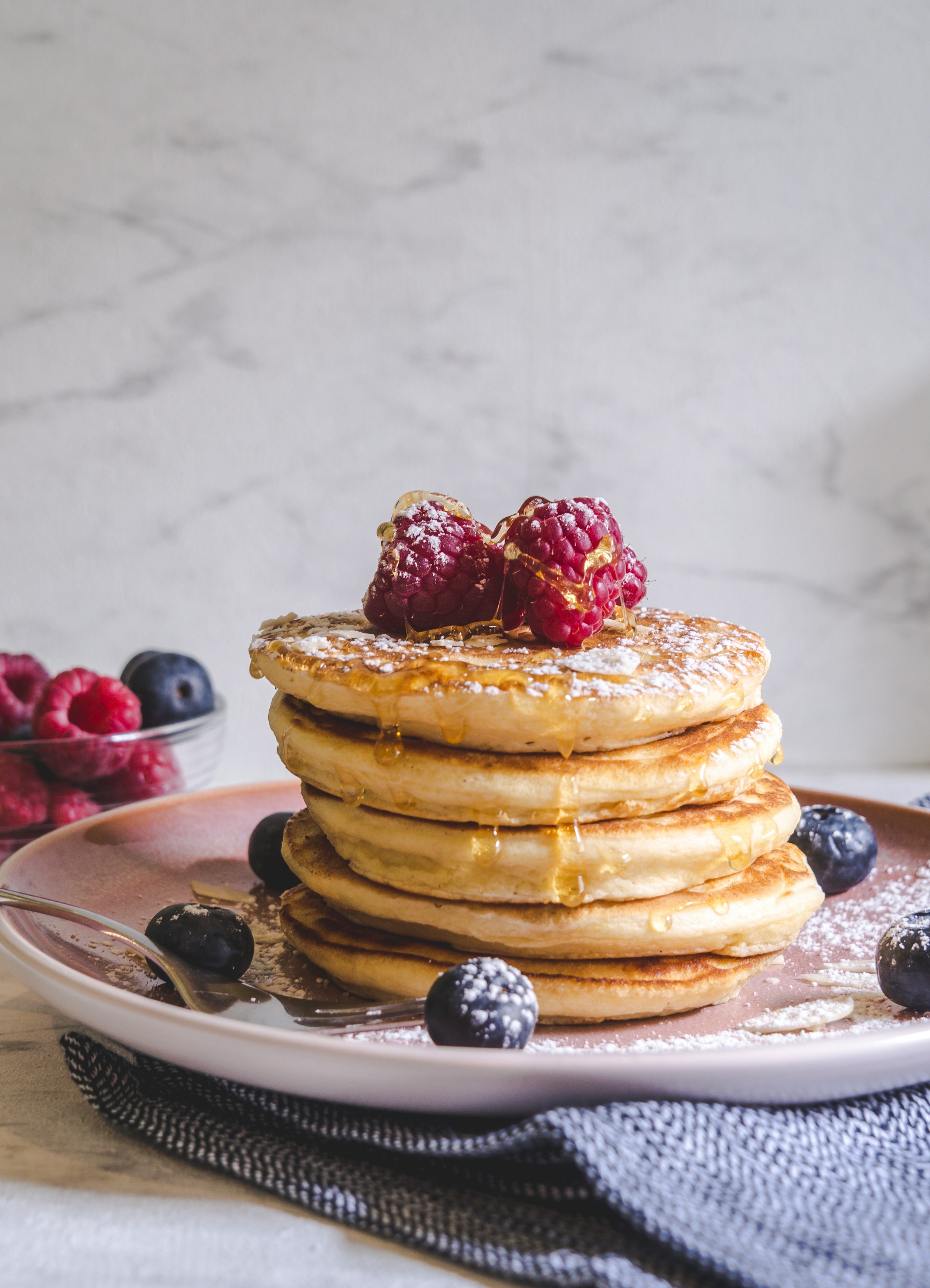 A photo showing pancakes with berries lying on a white ceramic plate | Source: Unsplash