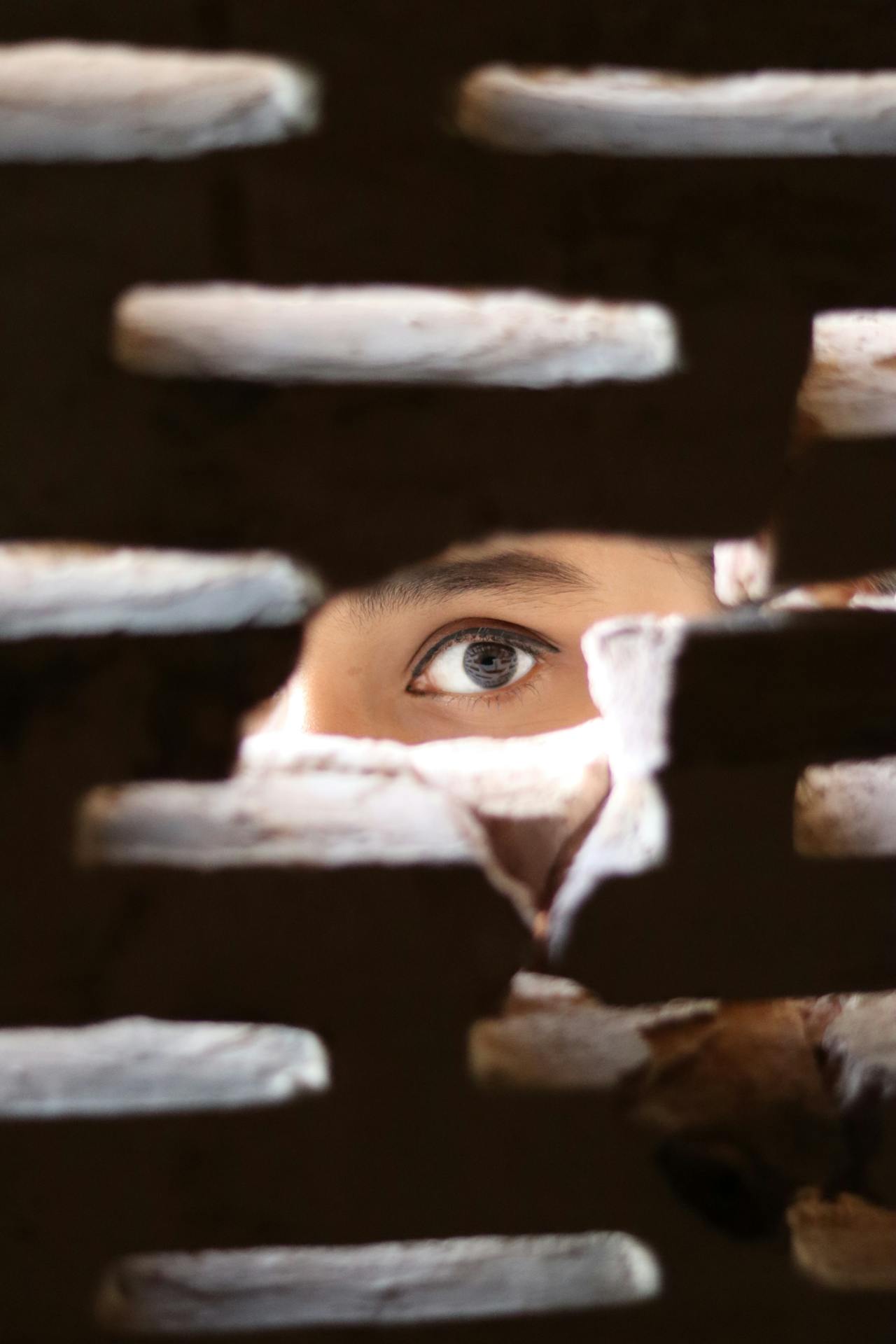A terrified woman peeking through a hole in the wall | Source: Pexels