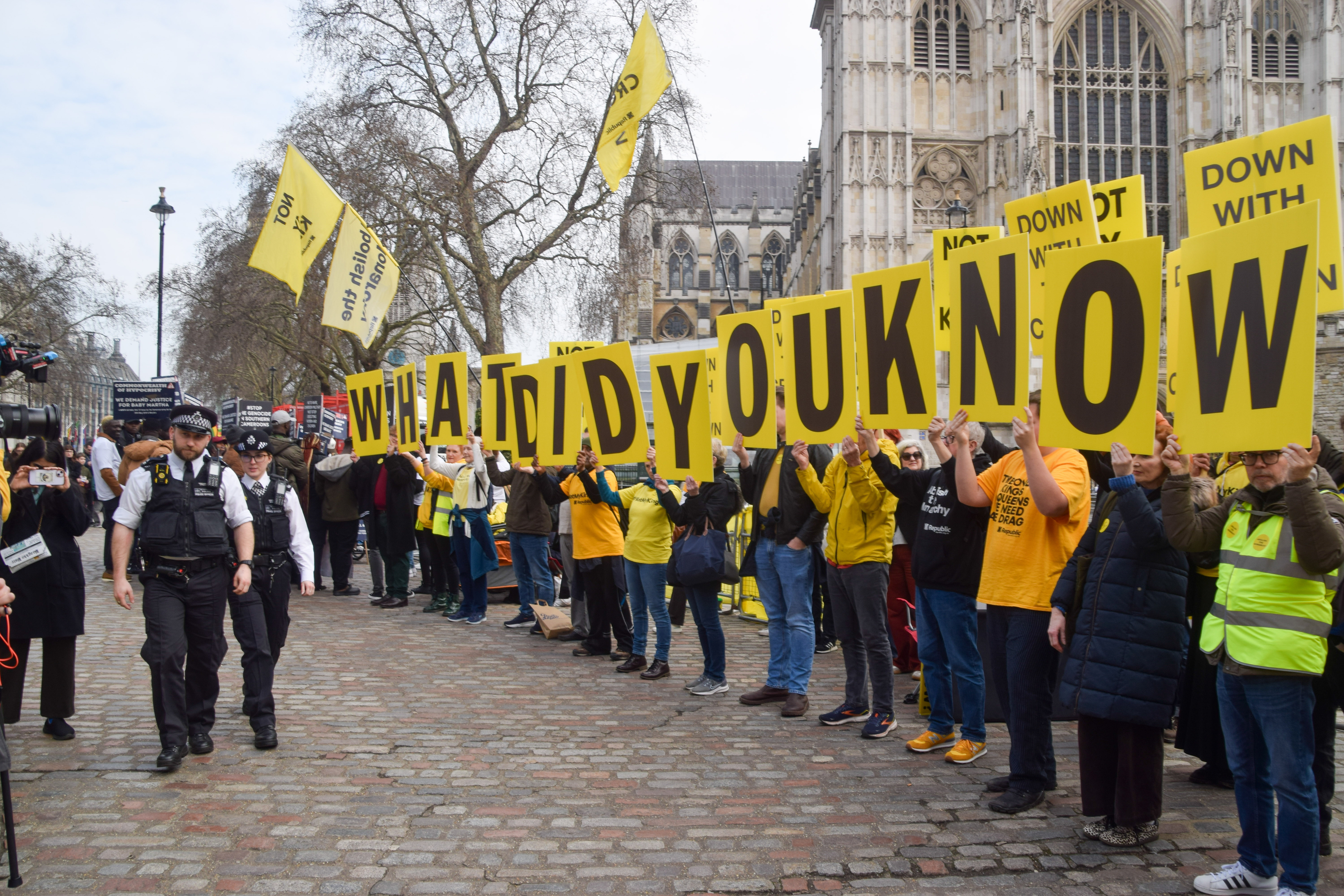 Police officers walk past activists from the anti-monarchy group Republic holding “What Did You Know?” placards referencing Andrew Mountbatten-Windsor and the Jeffrey Epstein scandal during a protest outside Westminster Abbey ahead of the Commonwealth Day Service on March 9, 2026. | Source: Getty Images