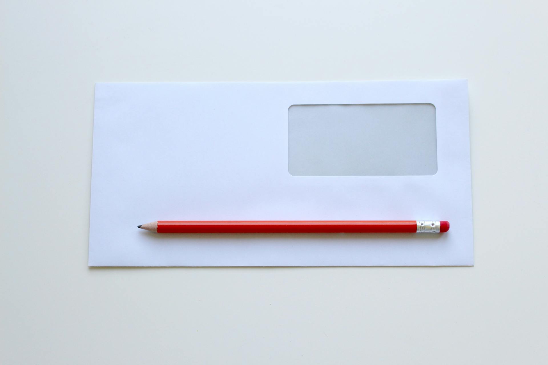 Red pencil lying on a white envelope | Source: Pexels