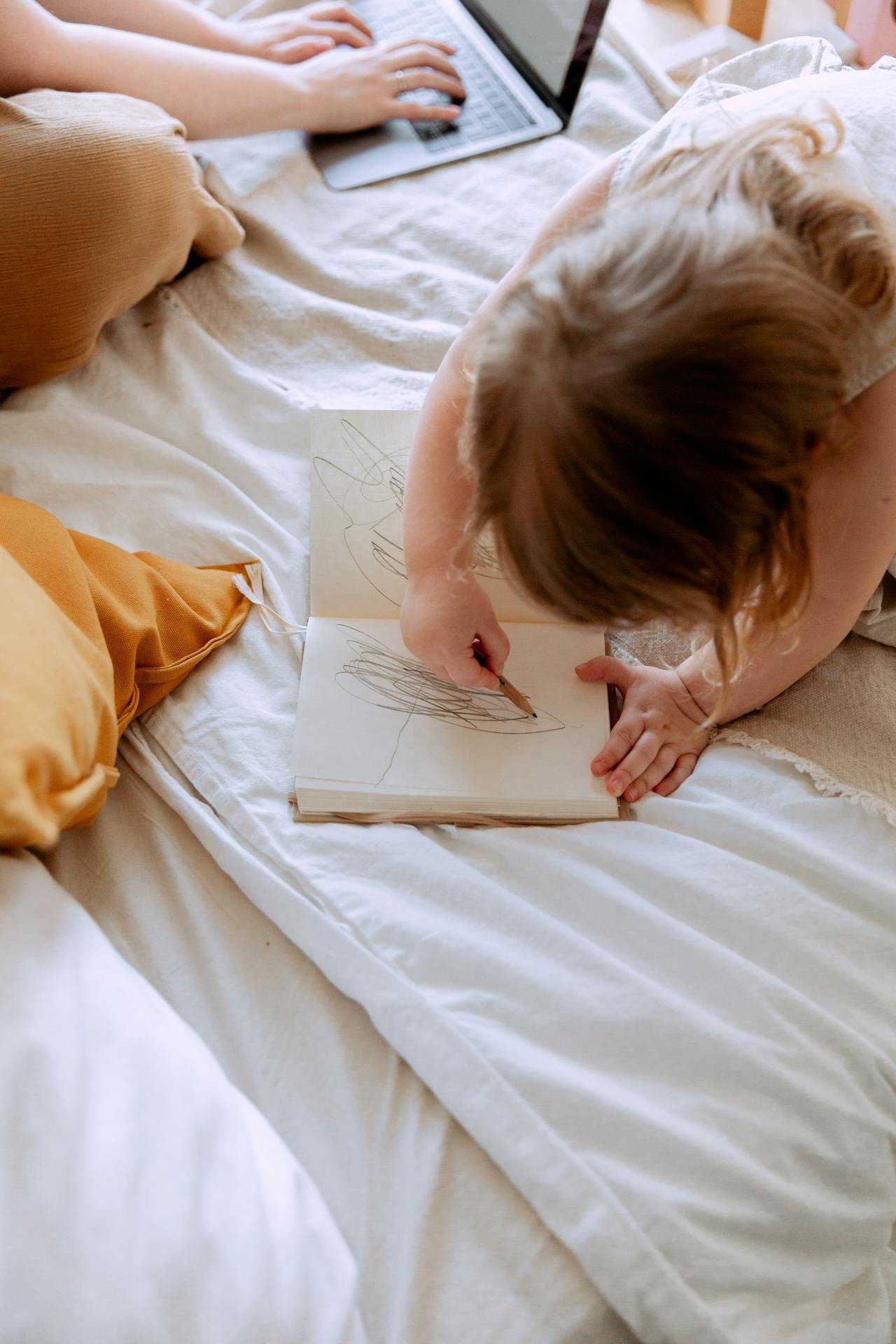Woman working on her laptop while her little daughter is scribbling on a notebook | Source: Pexels