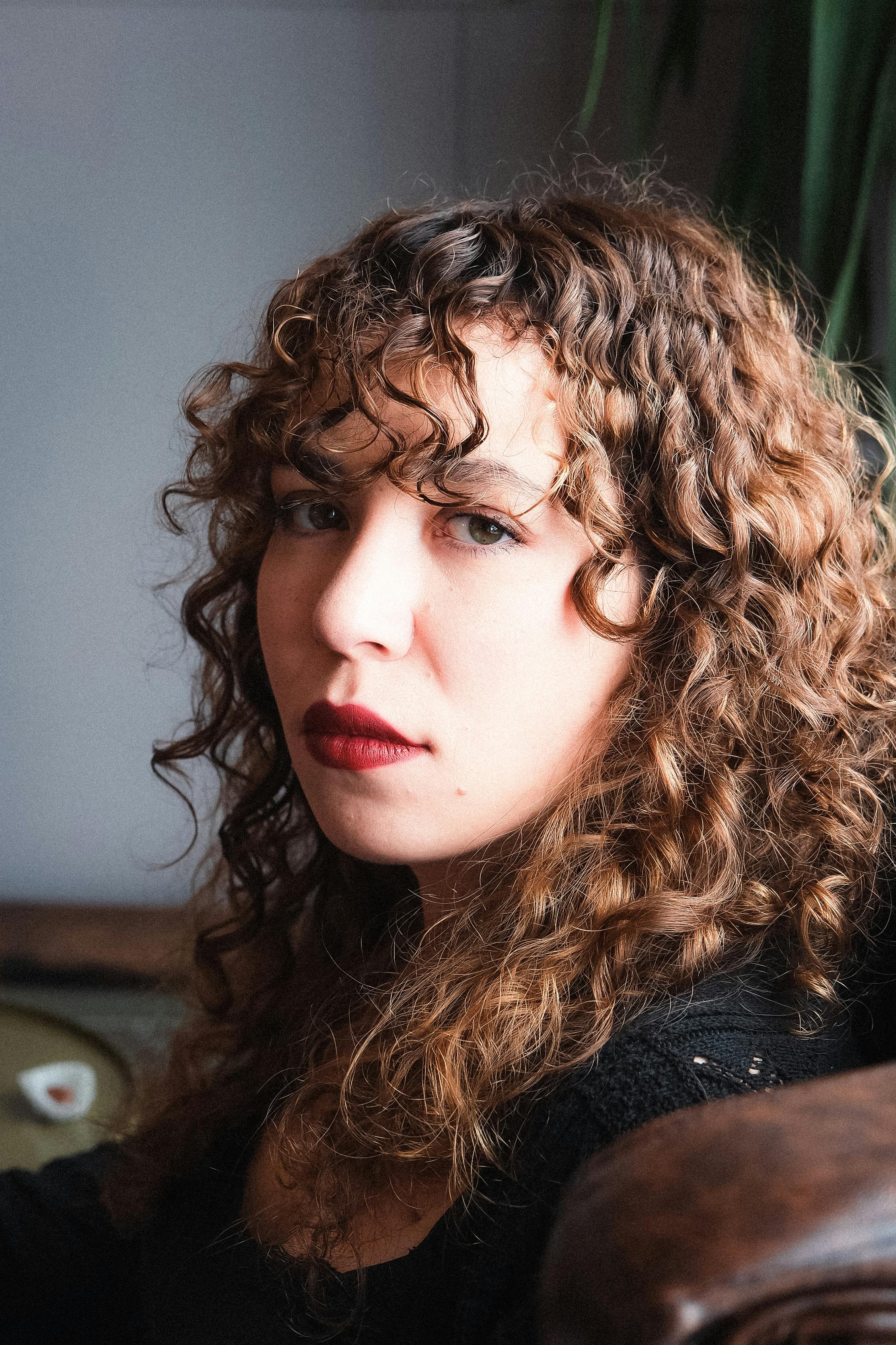 A pensive woman with curly hair and red lipstick | Source: Pexels