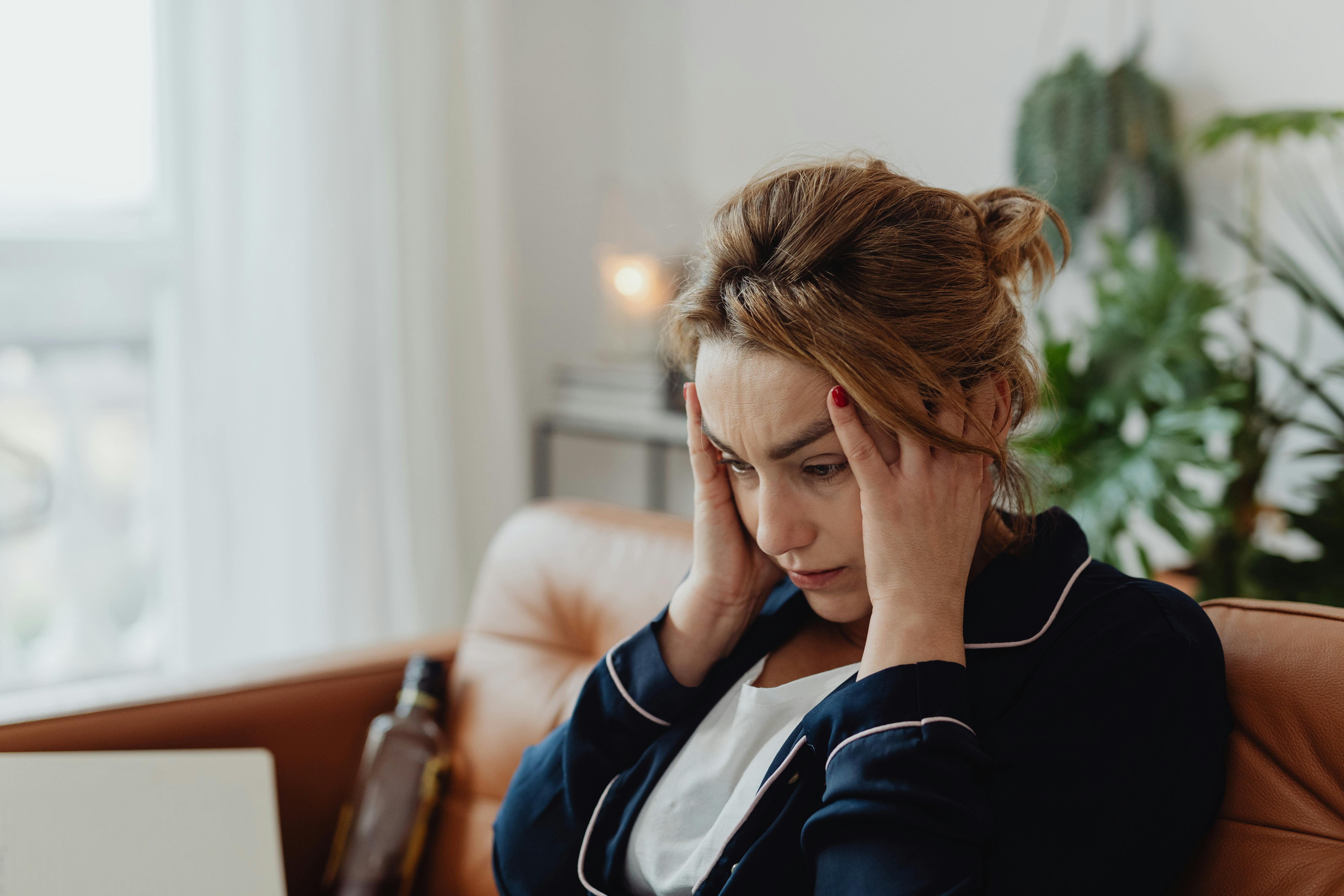 A woman sitting on a couch and holding her head | Source: Pexels