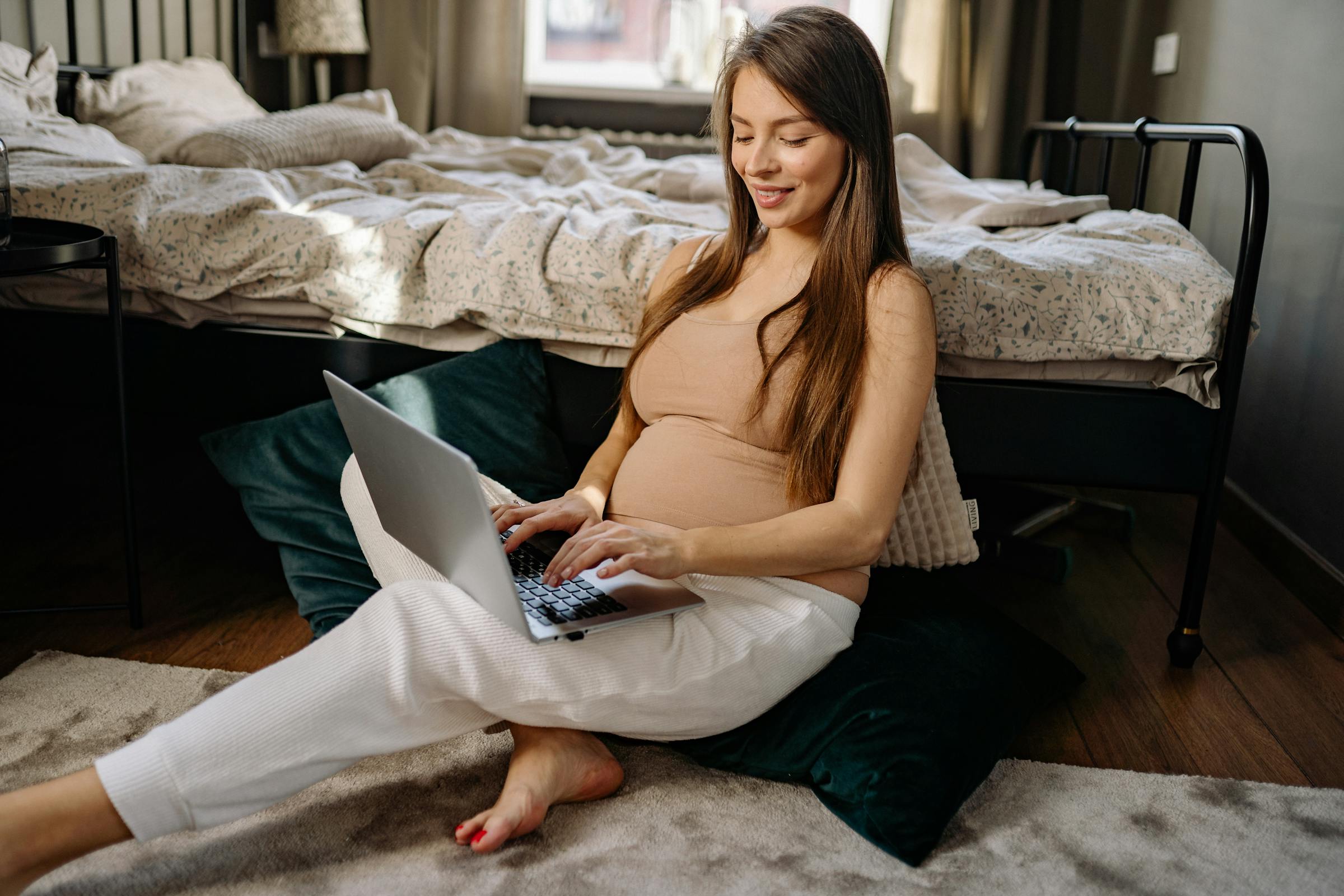 A pregnant woman working on a laptop with no wedding ring on her finger | Source: Pexels