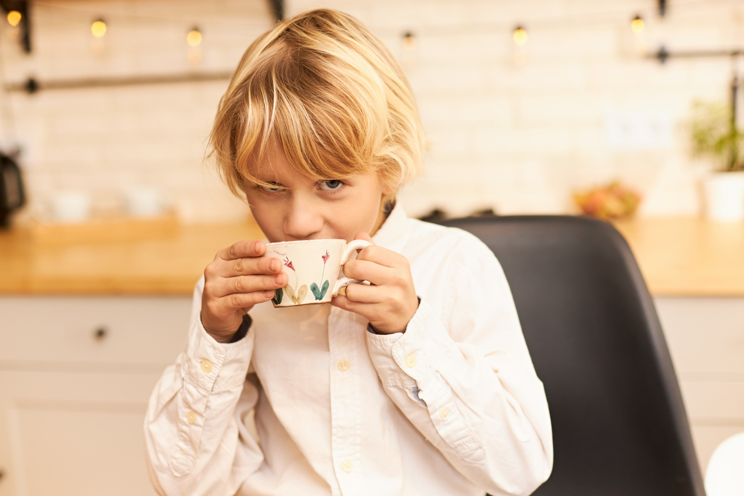 A little boy drinking from a ceramic cup while staring curiously | Source: Freepik