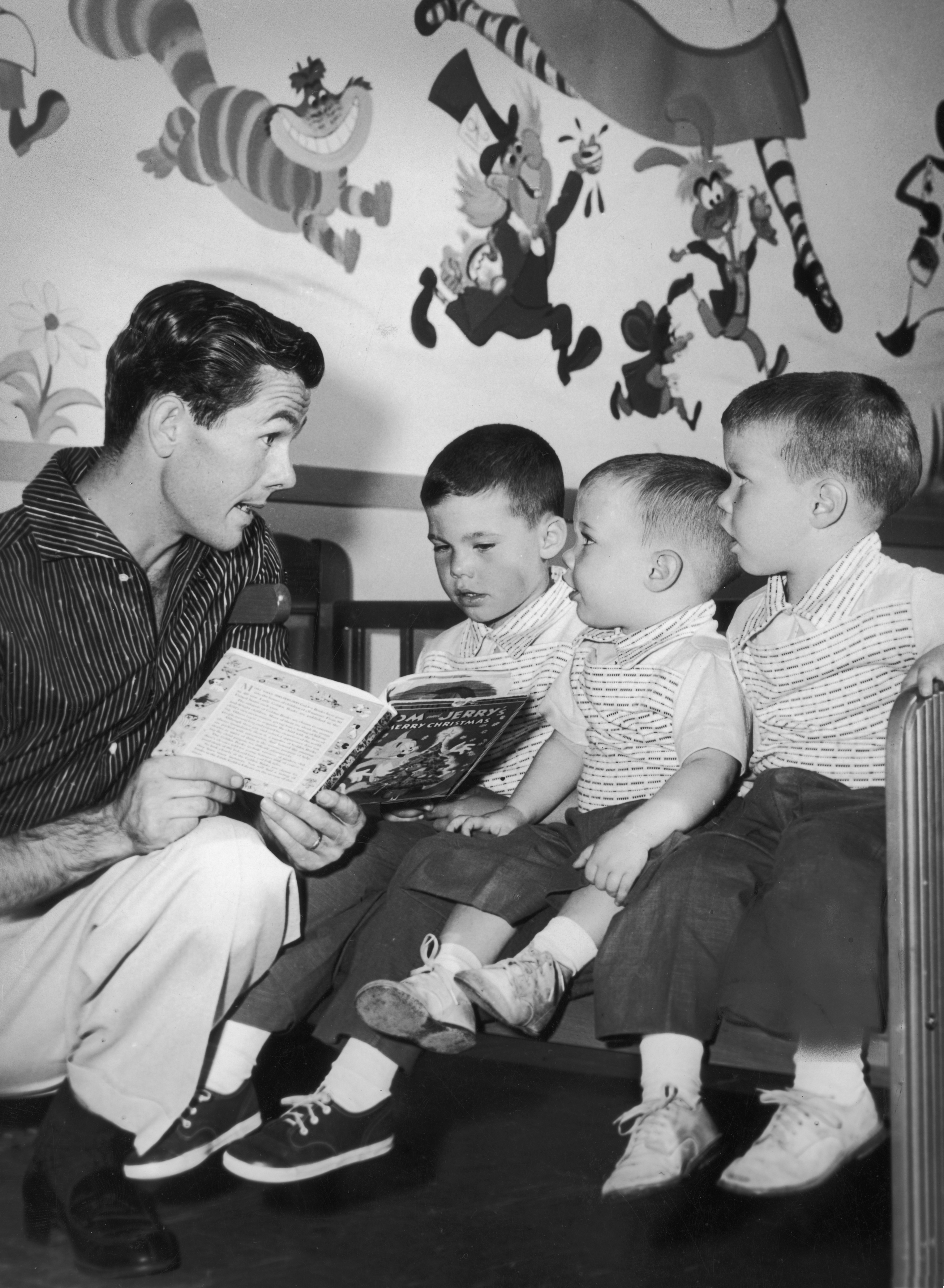 Johnny Carson kneels while he reads a children's book to his sons, Kit, Cory and Ricky, in their nursery, circa 1955. | Source: Getty Images