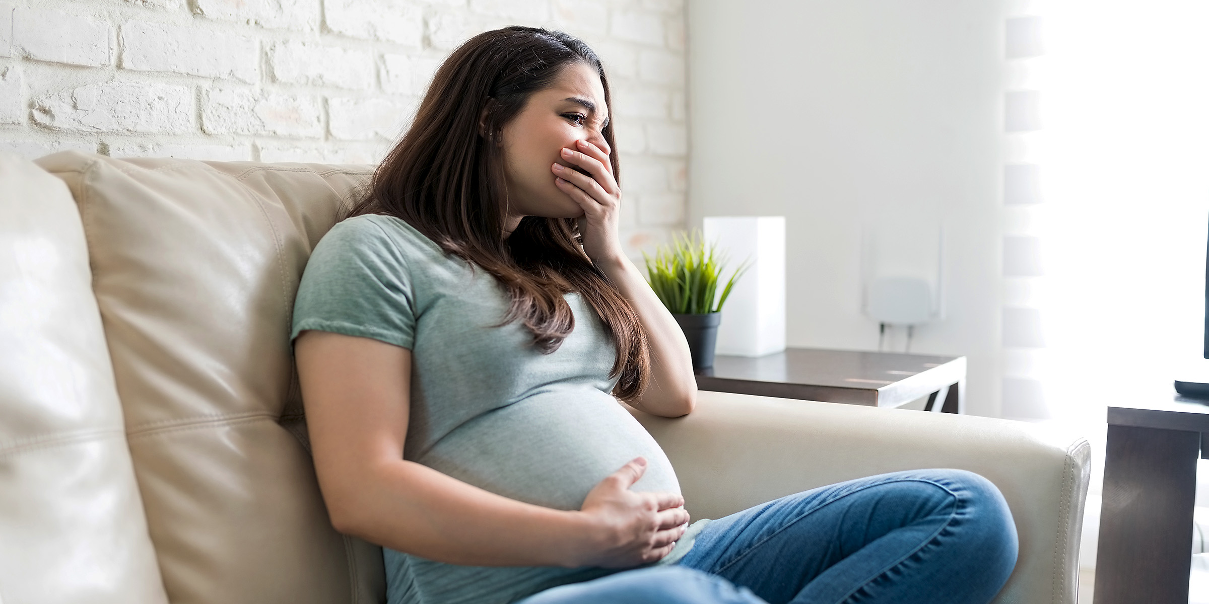 An upset pregnant woman sitting on a couch | Source: Shutterstock