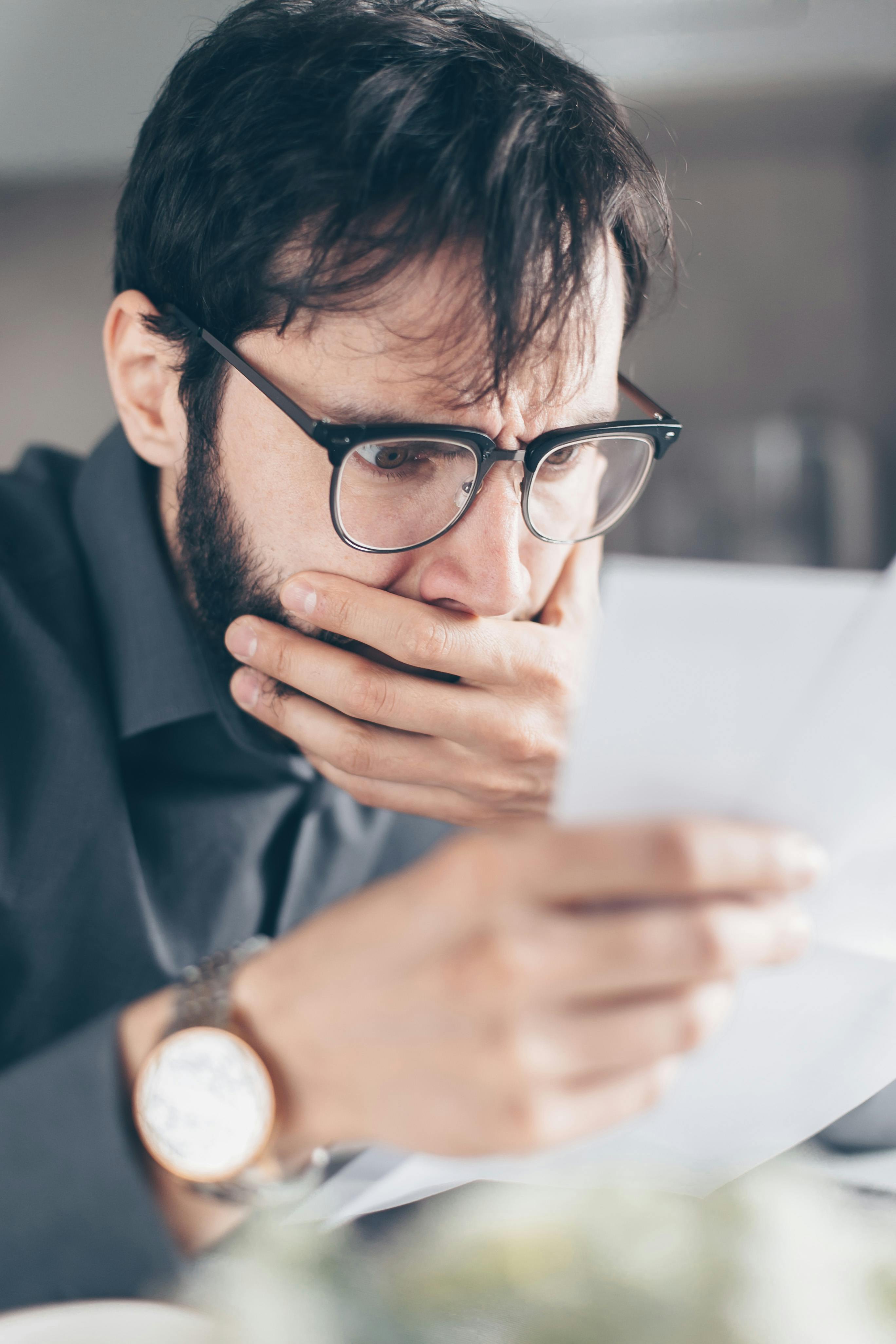 A shocked man covering his mouth while looking at papers | Source: Pexels