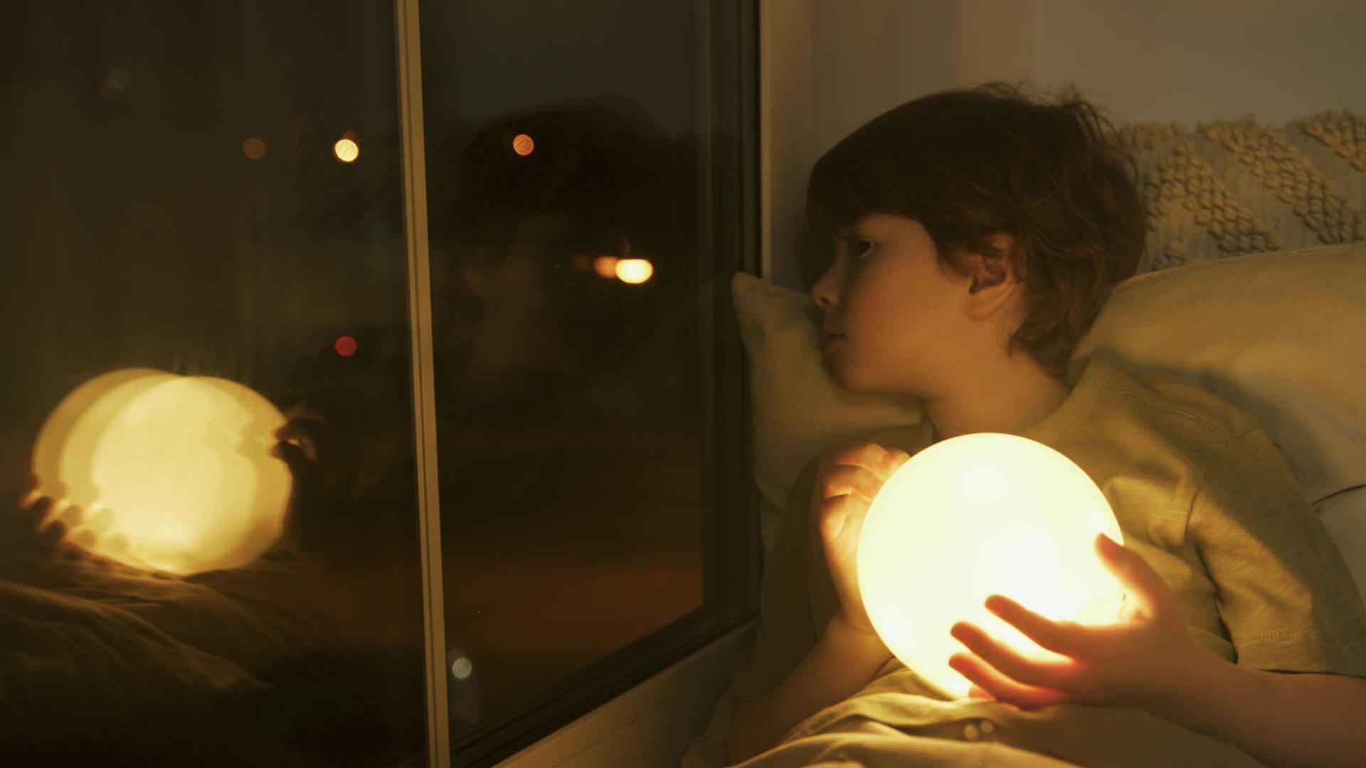 A young boy holding a ball of light and looking out the window | Source: Pexels