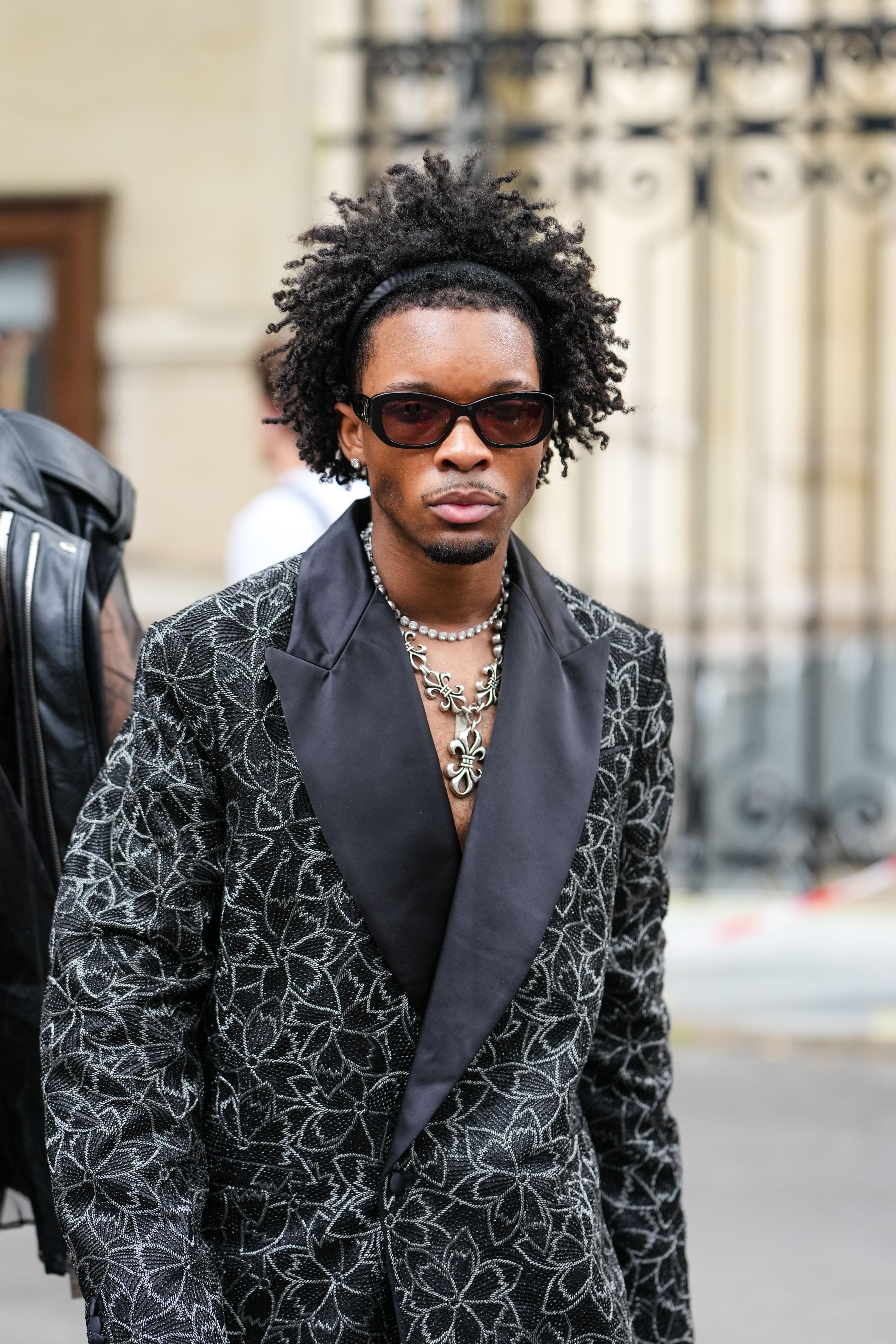 d4vd wears black Chanel sunglasses, diamond stud earrings, white gold diamond choker, silver Chrome hearts necklace, black silver floral beaded oversized Amiri blazer jacket, outside Amiri, during the Paris Fashion week Men's Spring/Summer 2026 on June 26, 2025 in Paris, France. | Source: Getty Images