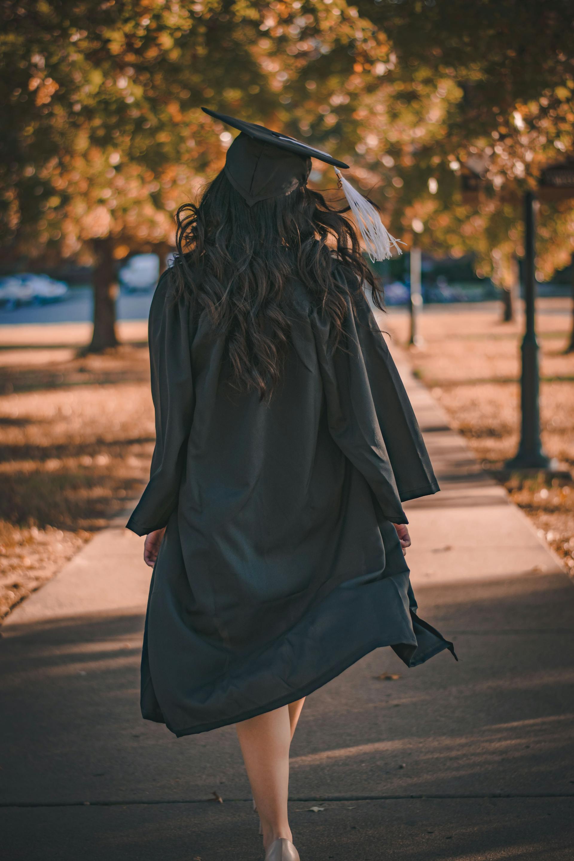 A woman wearing a cap and gown walking down a path | Source: Pexels