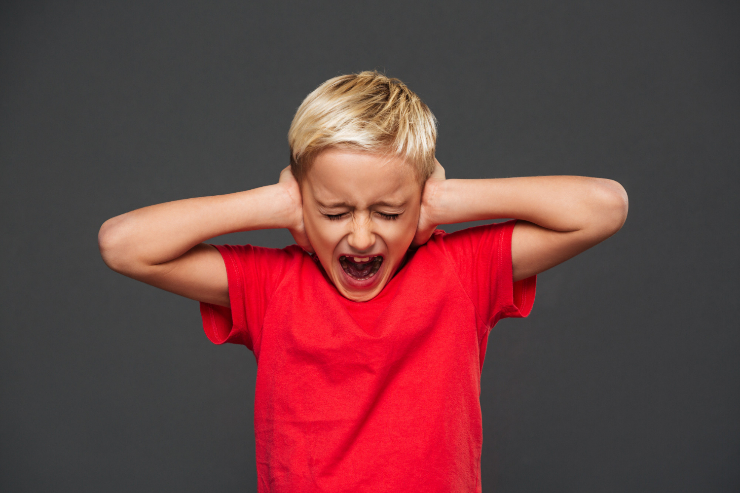 A young boy screaming while covering his ears | Source: Freepik