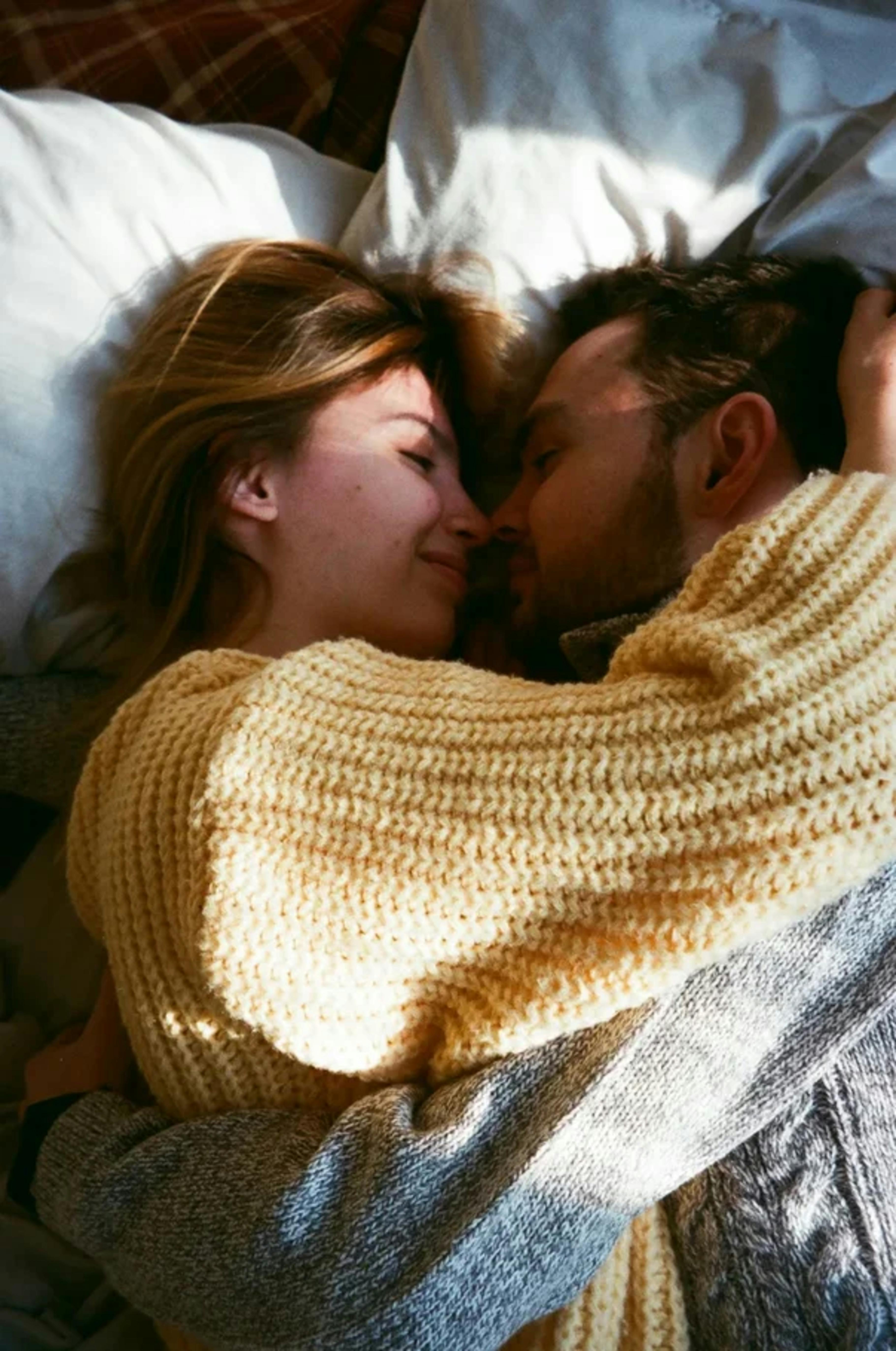 A couple cuddling on a bed in cozy sweaters | Source: Pexels