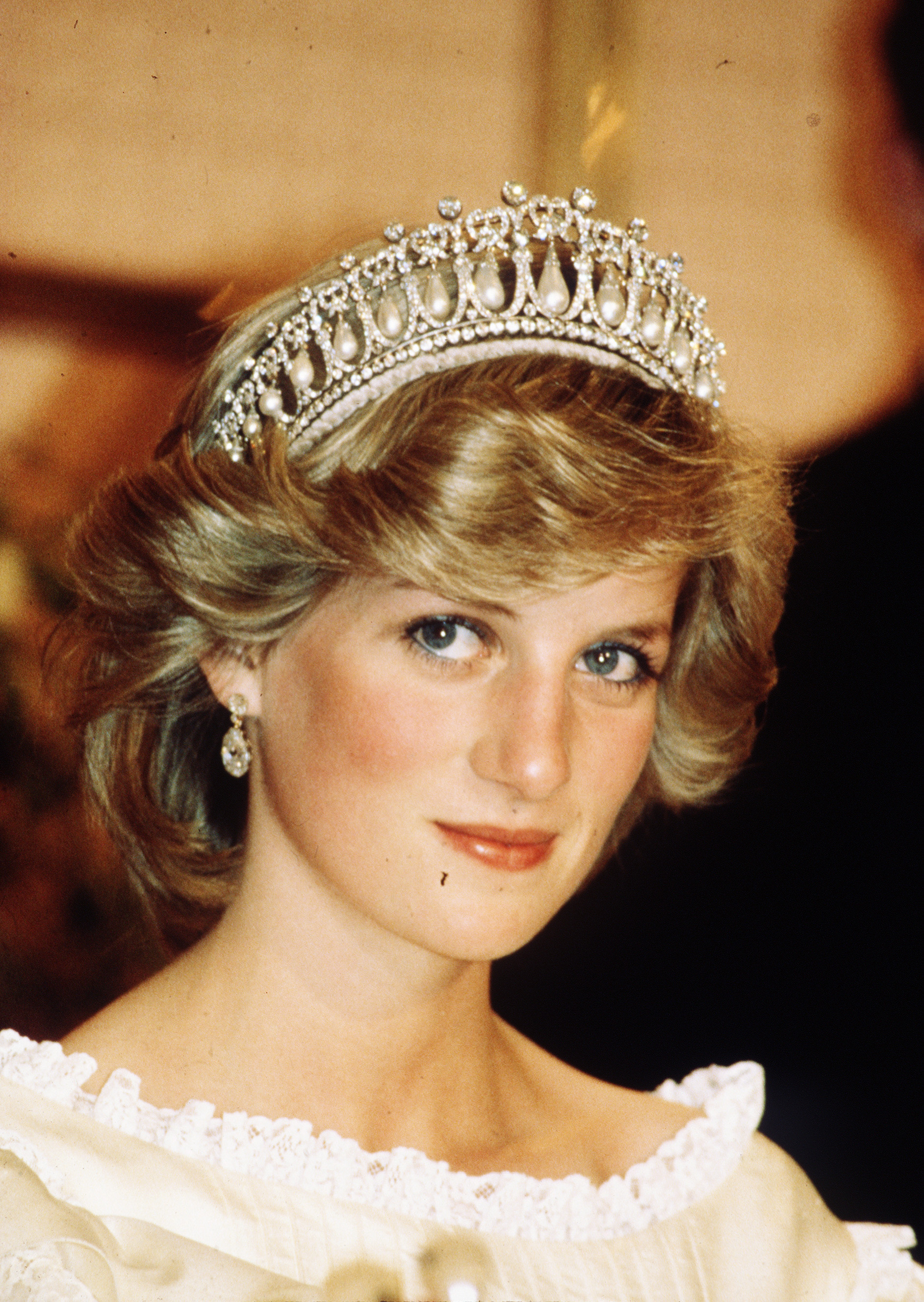 Diana, Princess of Wales, wearing a cream satin dress by Gina Fratini with the Queen Mary Cambridge Lover's Knot Tiara and diamond earrings attends a banquet on April 29, 1983, in Auckland, New Zealand. | Source: Getty Images