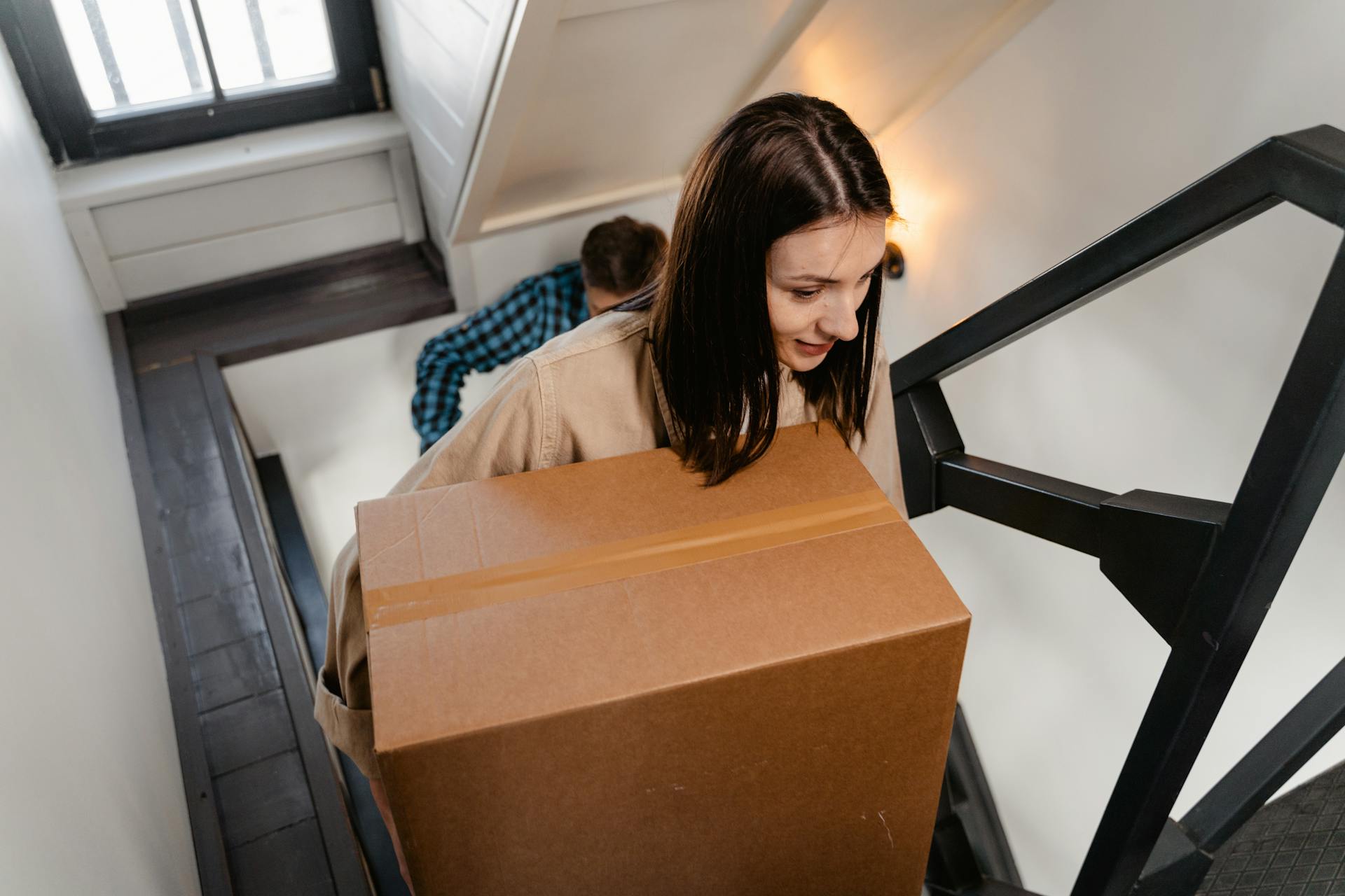 A woman carrying a box while ascending the stairs of her house | Source: Pexels