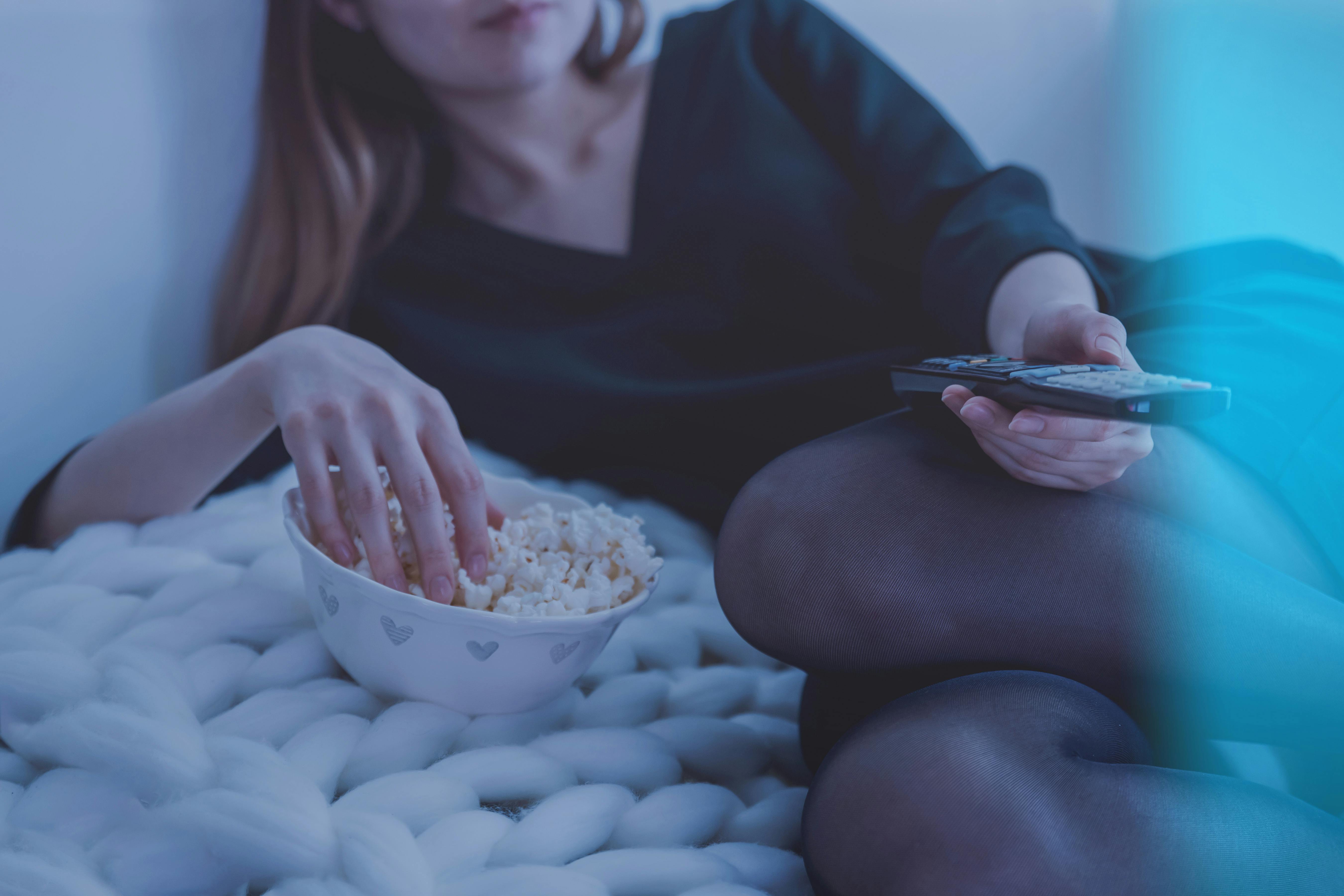 A woman eating a bowl of popcorn and holding a television remote | Source: Pexels