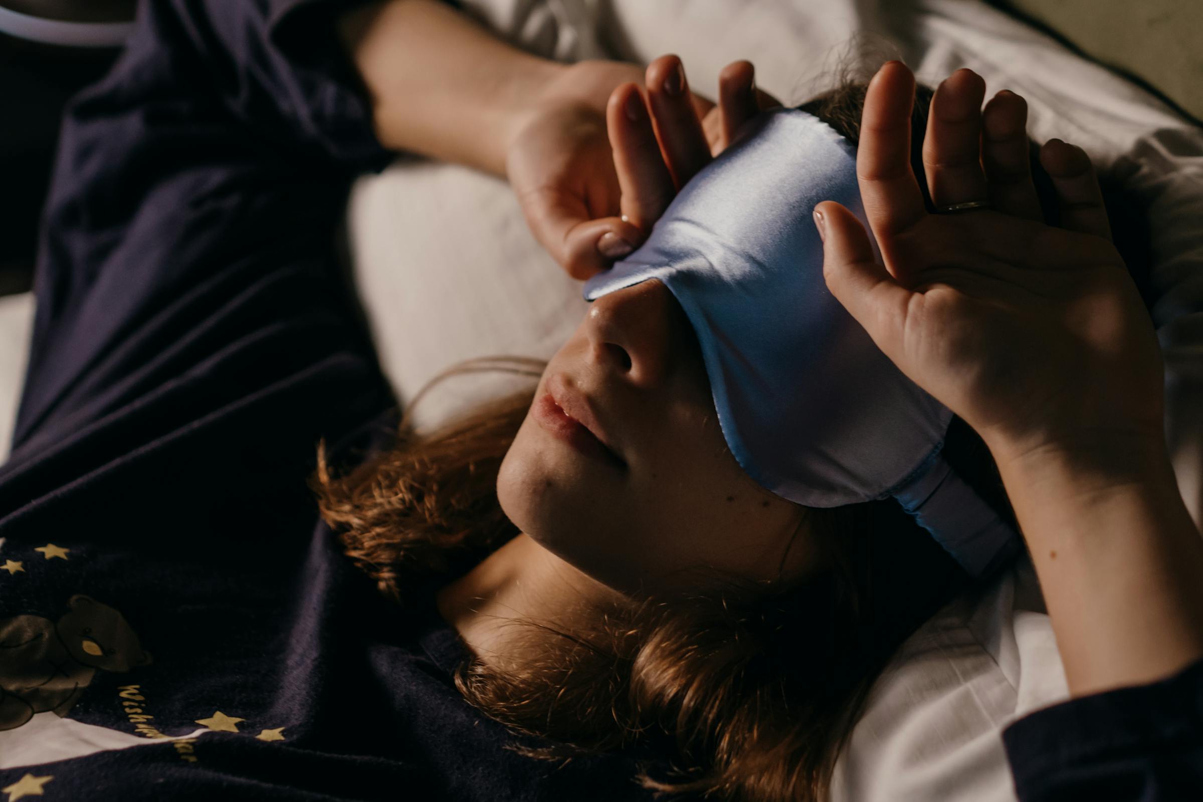 A woman wearing a sleep mask lies in bed but appears awake | Source: Pexels