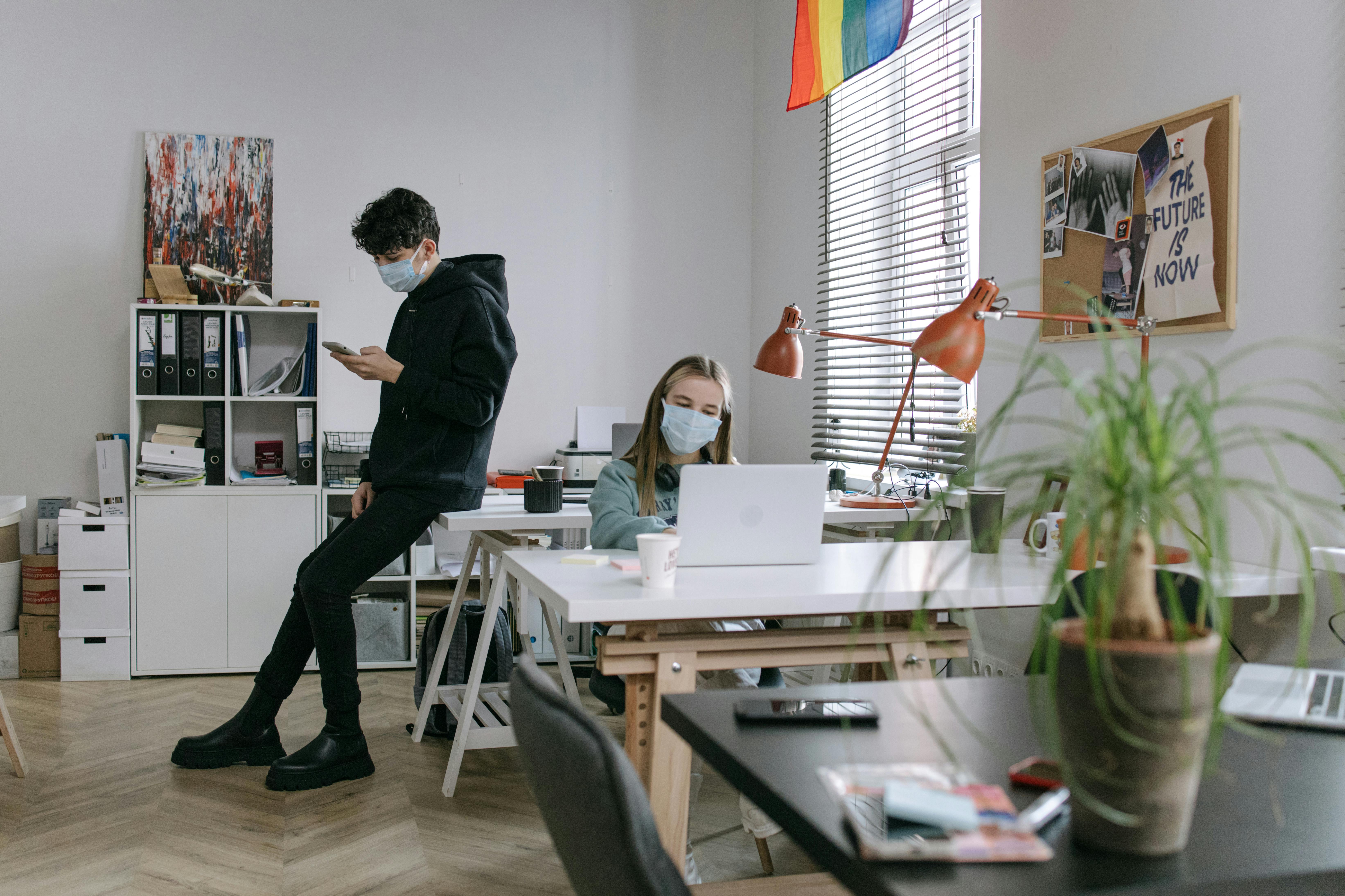 A man sitting on the office table with his back turned against a woman using a laptop | Source: Pexels