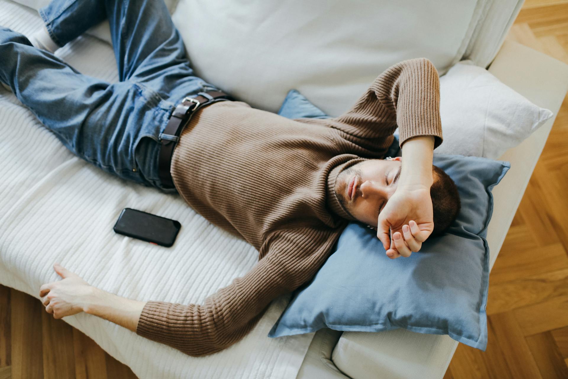 A man sleeping on the couch with his phone beside him | Source: Pexels