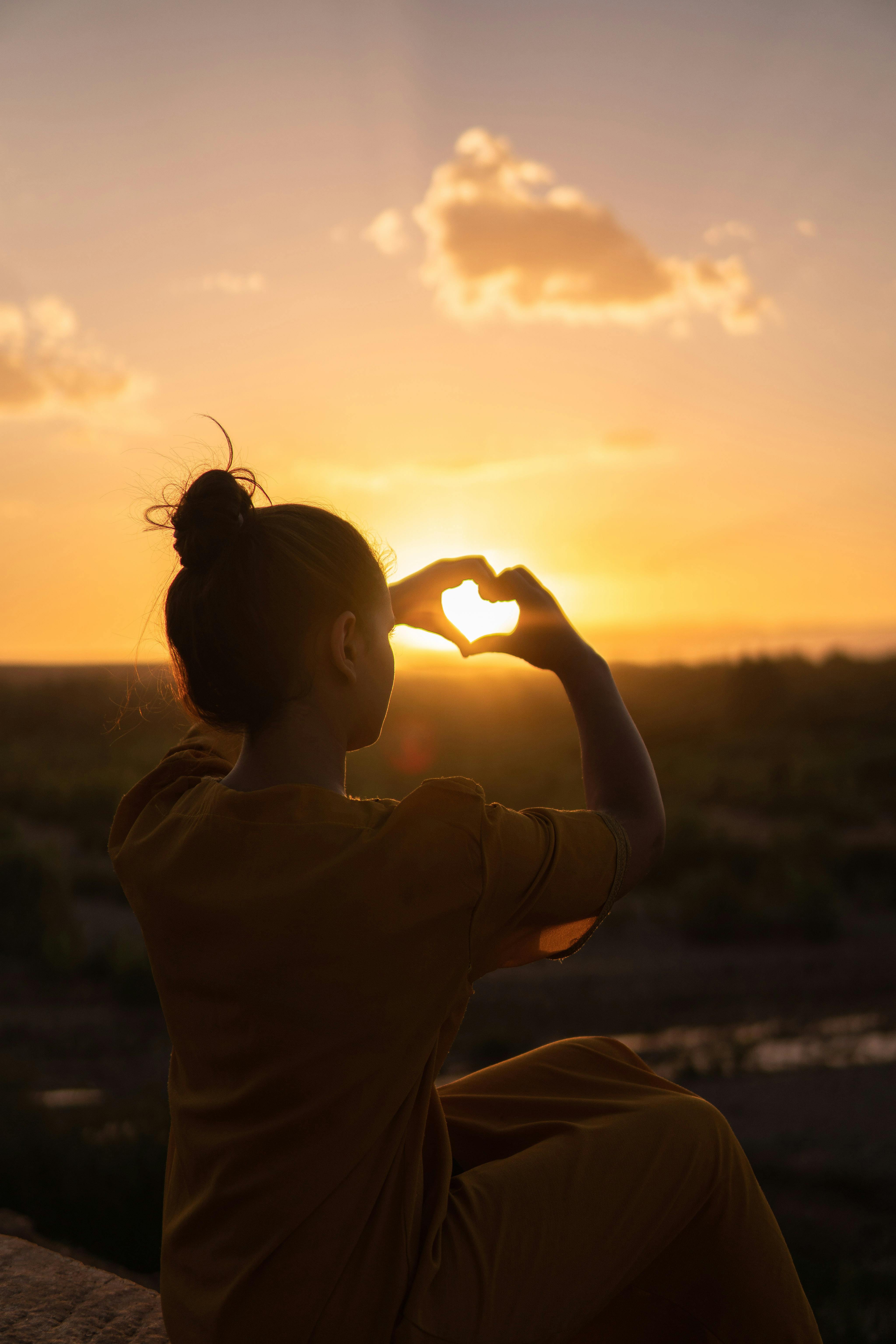 A woman making a heart shape at sunset | Source: Pexels