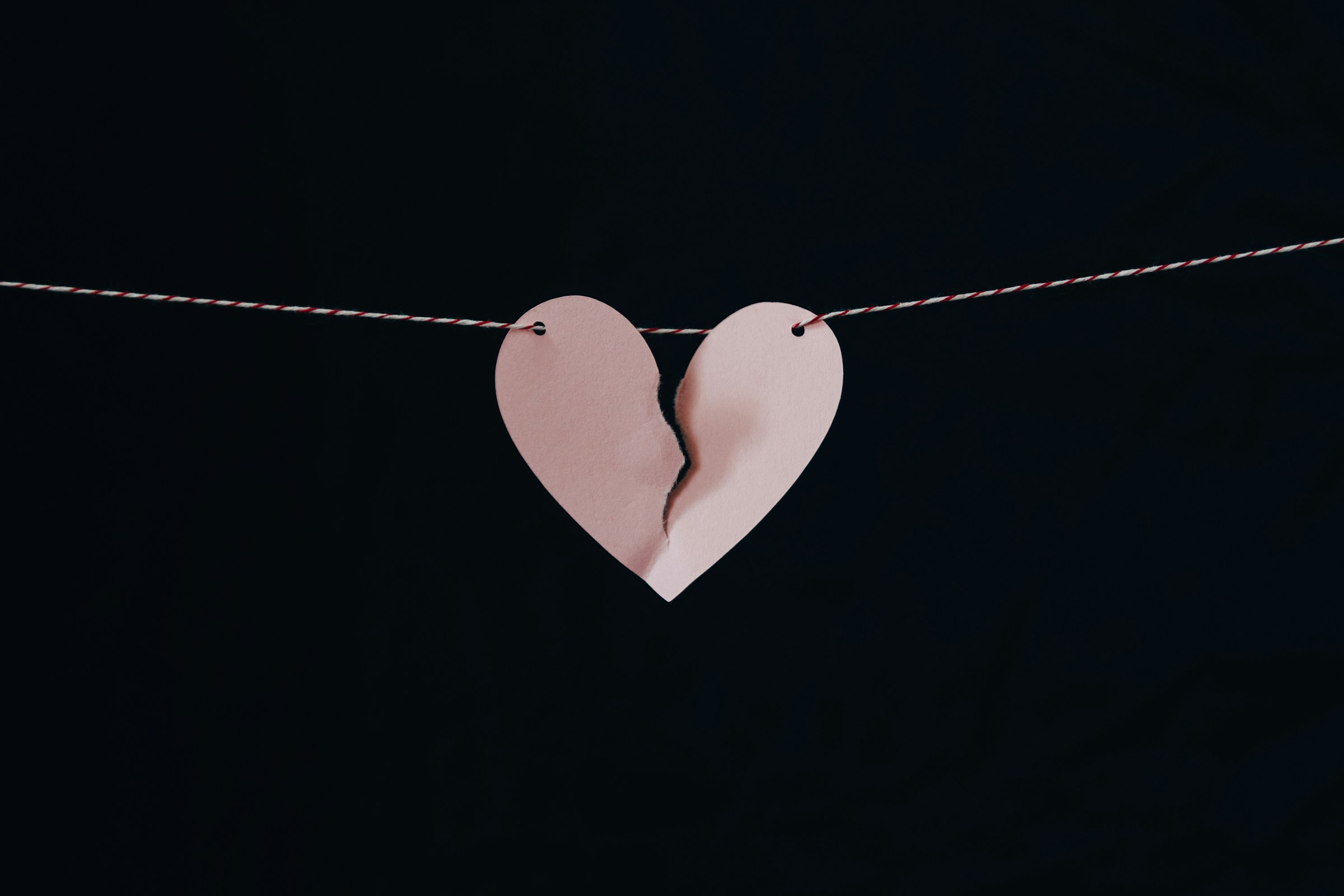 A broken pink paper heart hanging on a wire | Source: Unsplash
