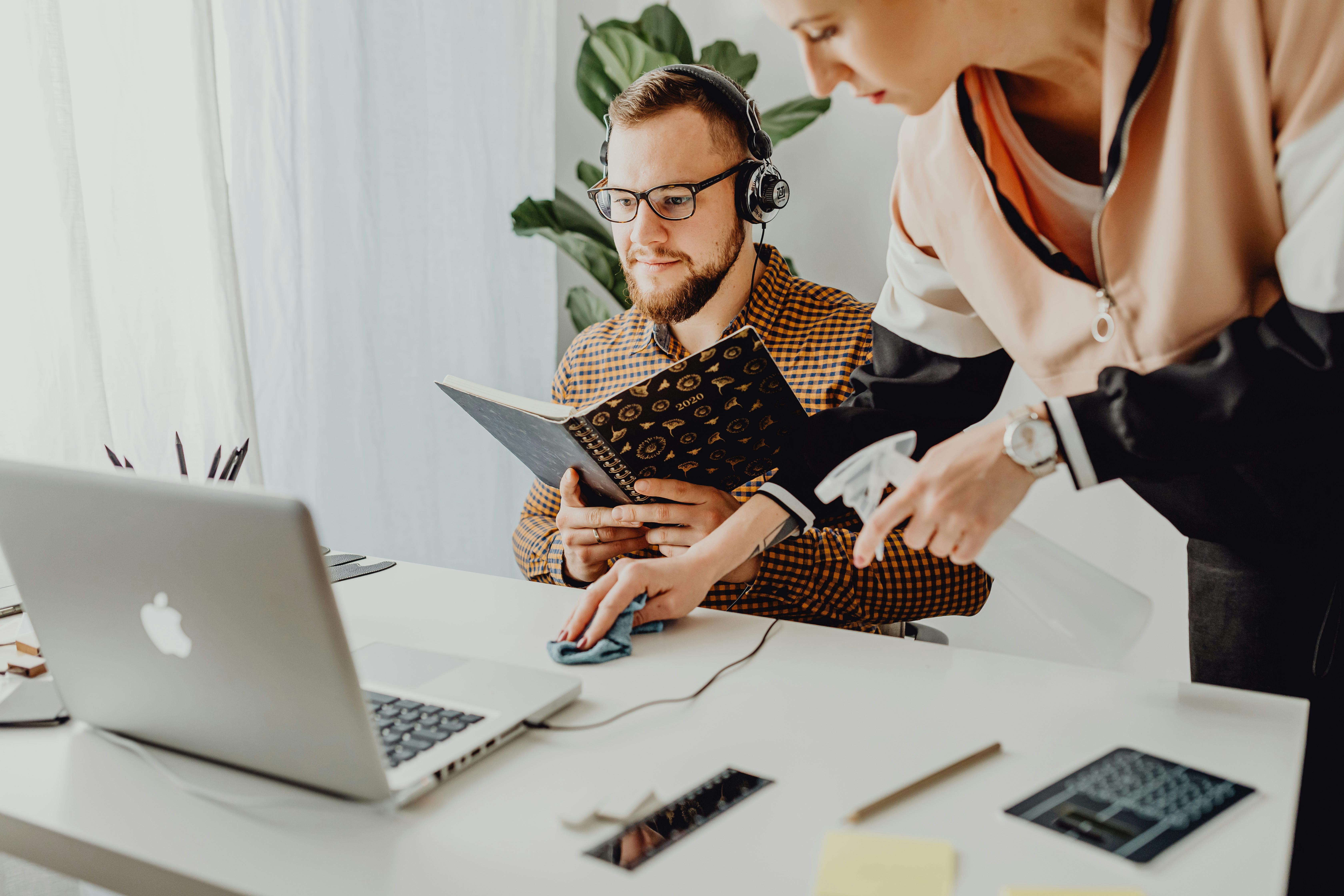 A woman wipes the table while a man holds a notebook | Source: Pexels