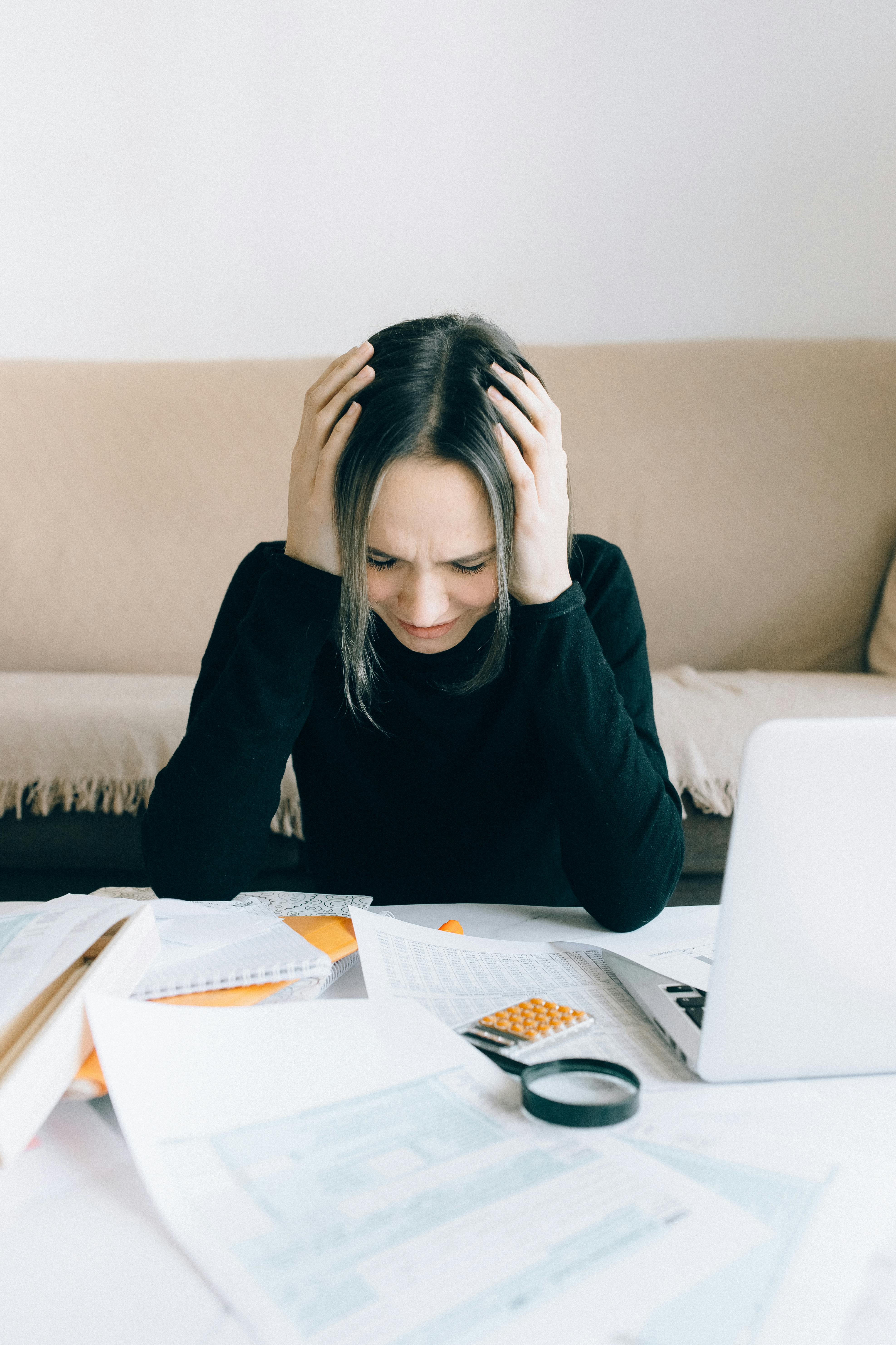 A woman sitting at a table and holding her head | Source: Pexels