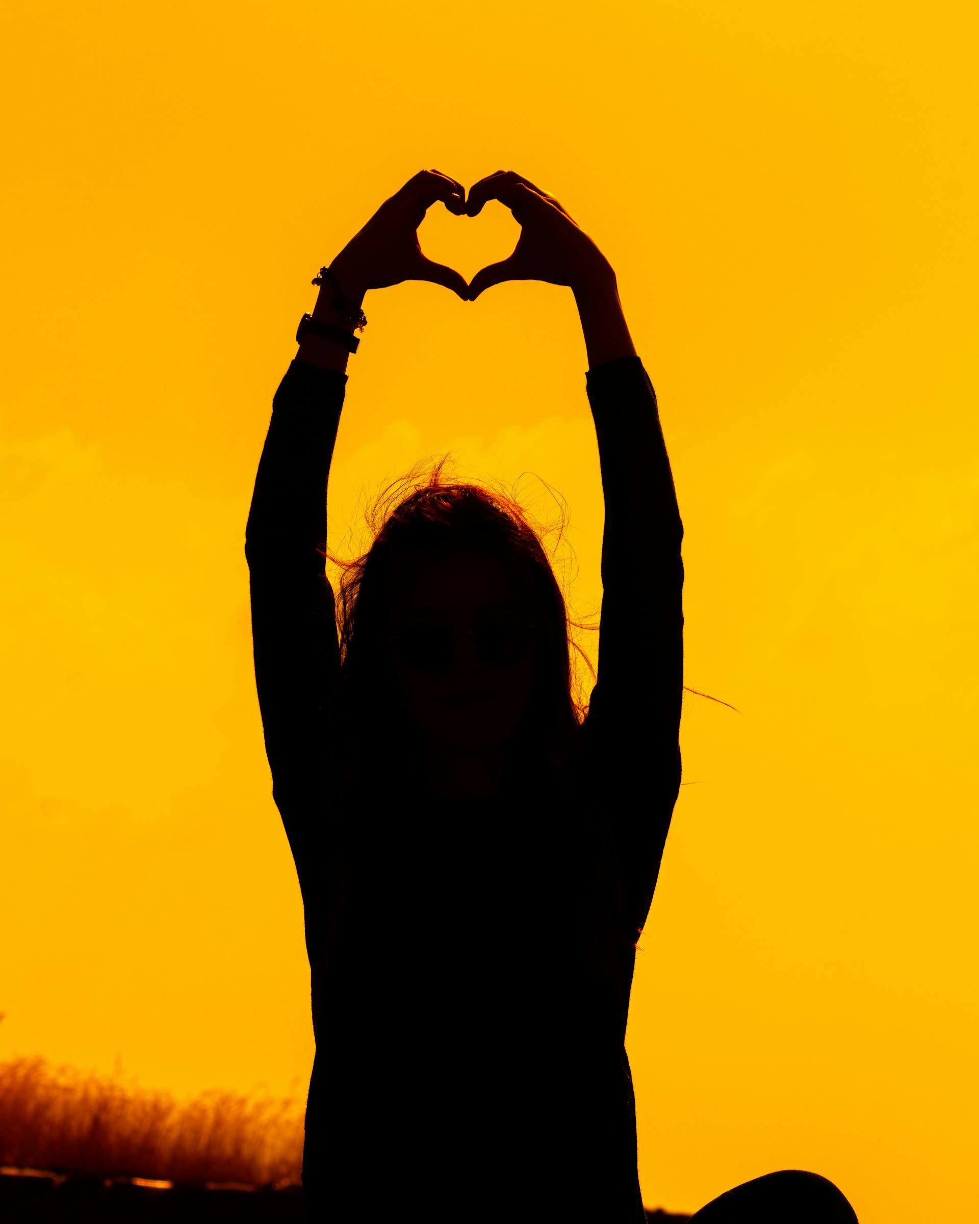 A woman's silhouette making a heart shape with her hands at sunset | Source: Pexels