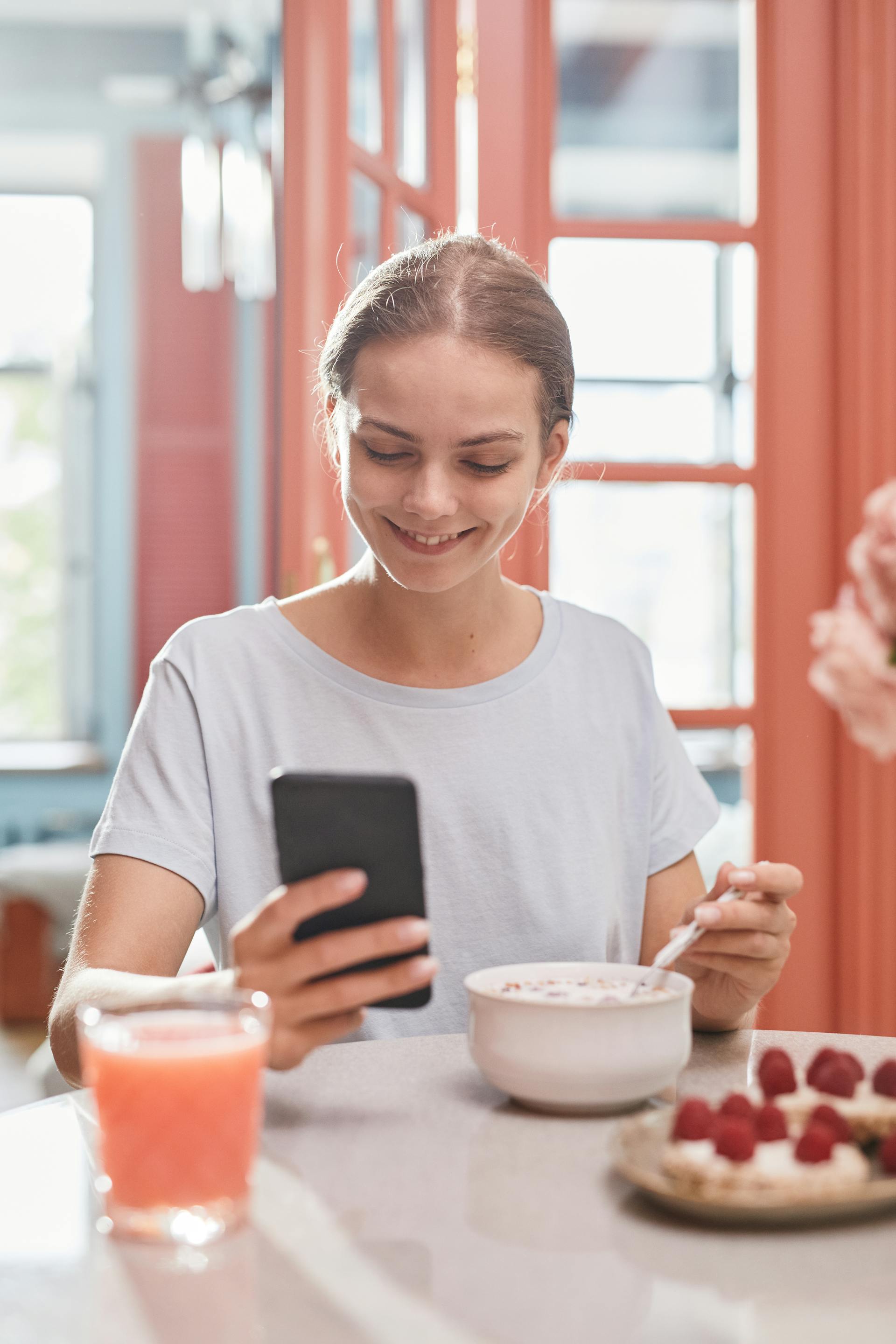 A woman smiling while eating breakfast and using a phone | Source: Pexels