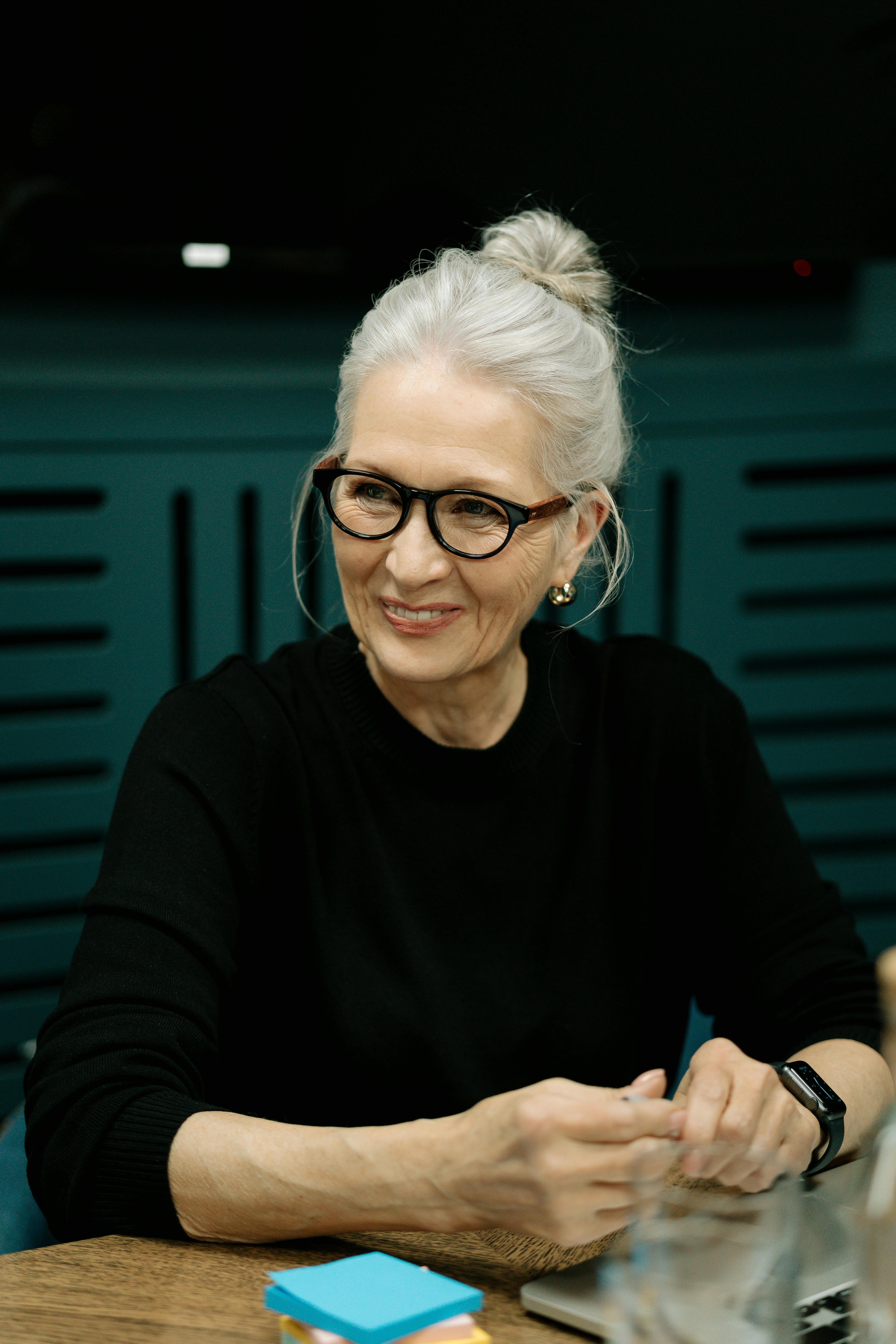 Une femme âgée souriante assise à une table | Source : Pexels