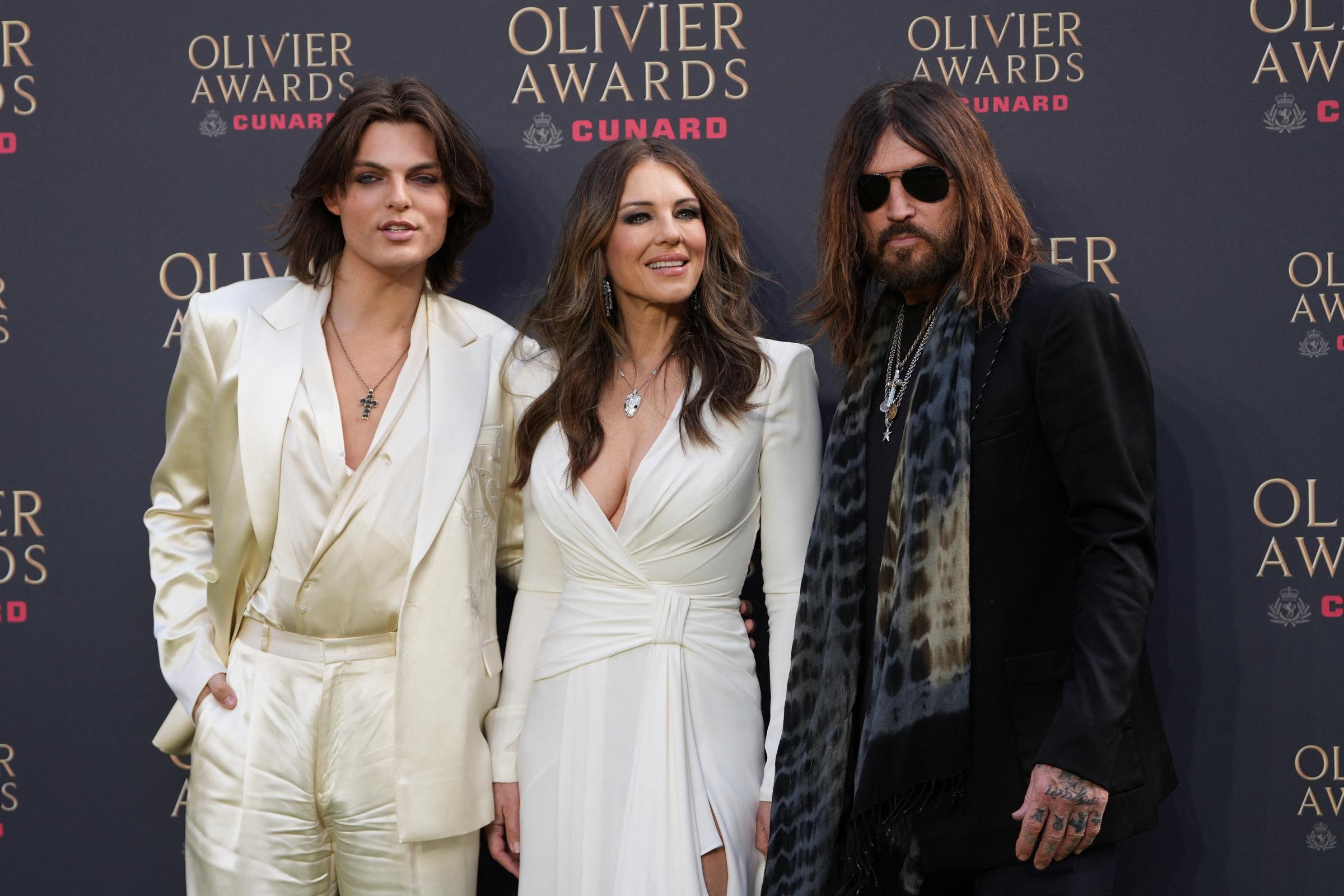 Damian Hurley, Elizabeth Hurley and Billy Ray Cyrus pose on the green carpet upon arrival to attend The Olivier Awards at the Royal Albert Hall in central London on April 12, 2026. | Source: Getty Images