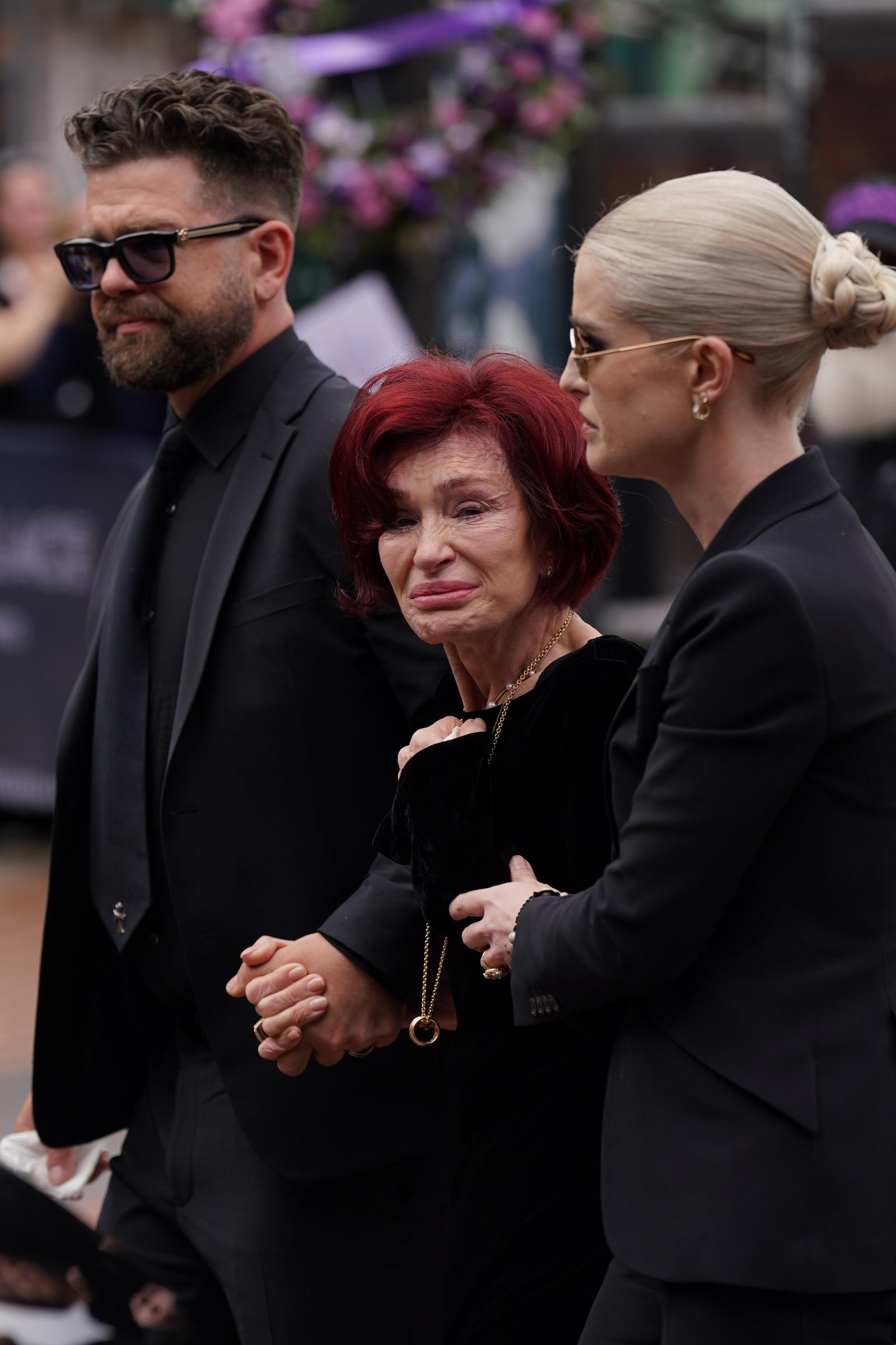 Jack, Sharon, and Kelly Osbourne approach the messages and floral tributes left at the Black Sabbath Bridge bench on Broad Street in Birmingham, in memory of Black Sabbath frontman Ozzy Osbourne, as his body is brought back to his home city for a procession following his death at age 76. Picture date: Wednesday July 30, 2025. | Source: Getty Images
