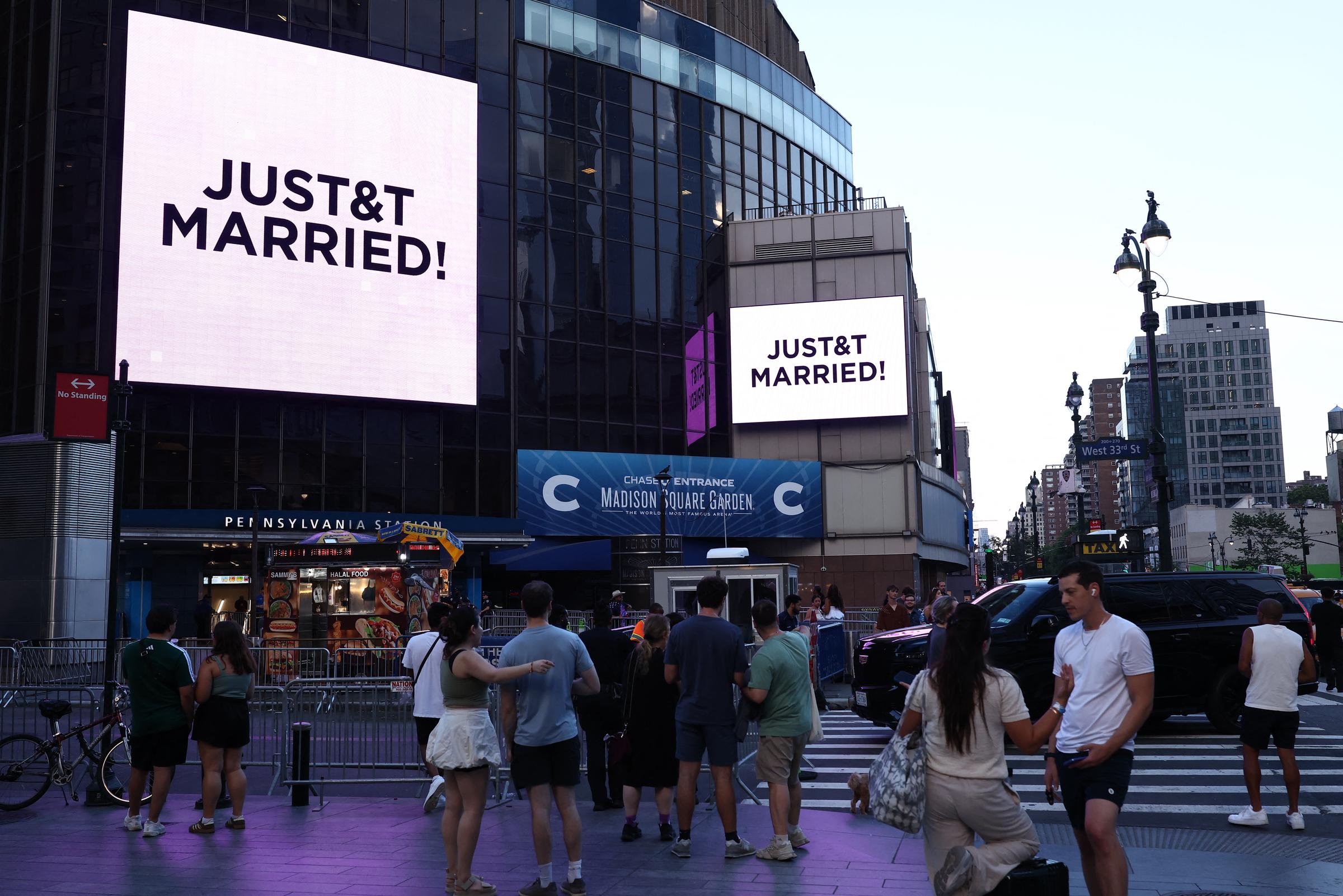 People watch giant screens showing the message "JUST&T MARRIED!" (T&T for Taylor and Travis) outside Madison Square Garden, the reported venue for the wedding celebrations of pop singer Taylor Swift and pro-athlete Travis Kelce, in New York City on July 3, 2026. | Source: Getty Images