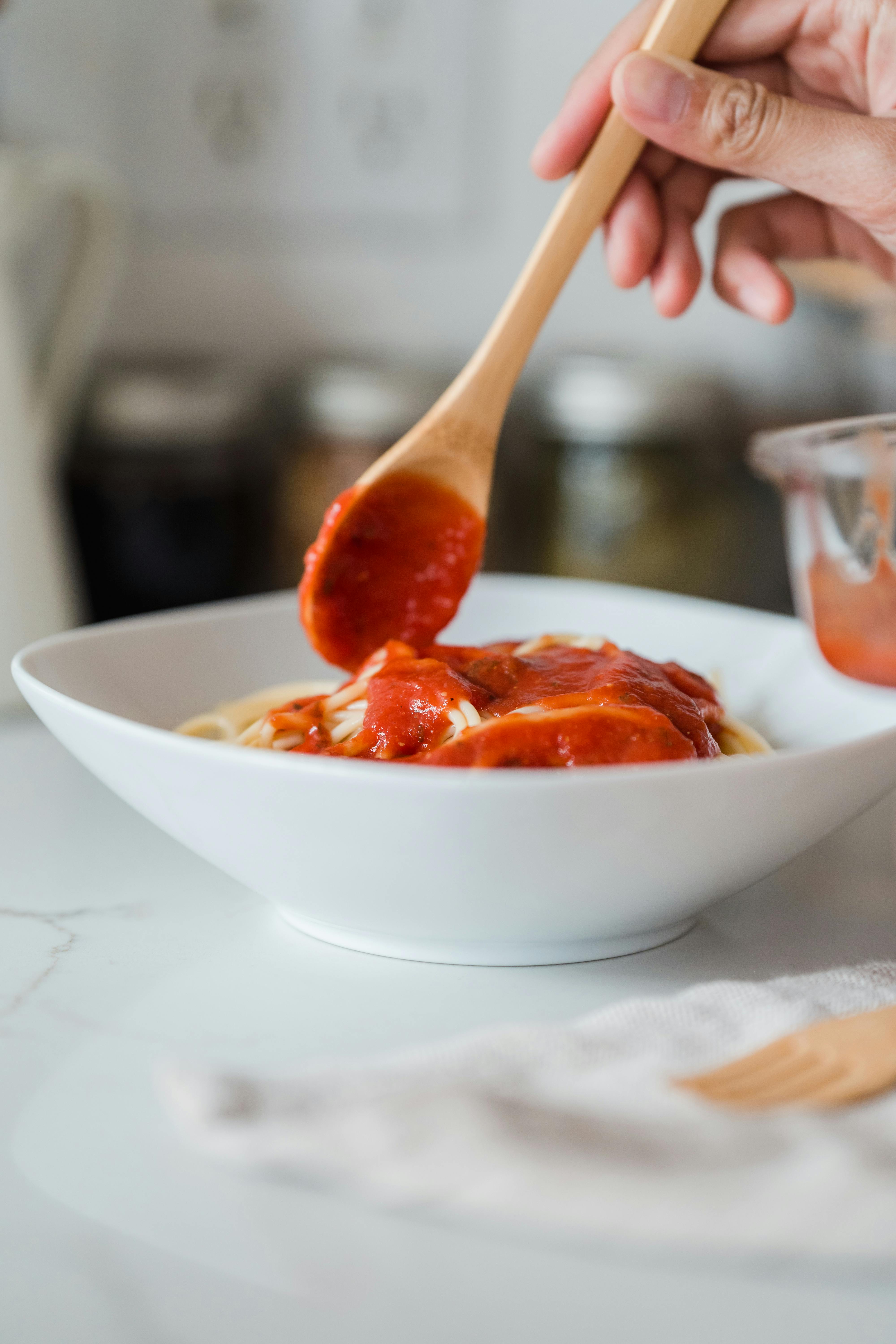 A person adding sauce to pasta | Source: Pexels