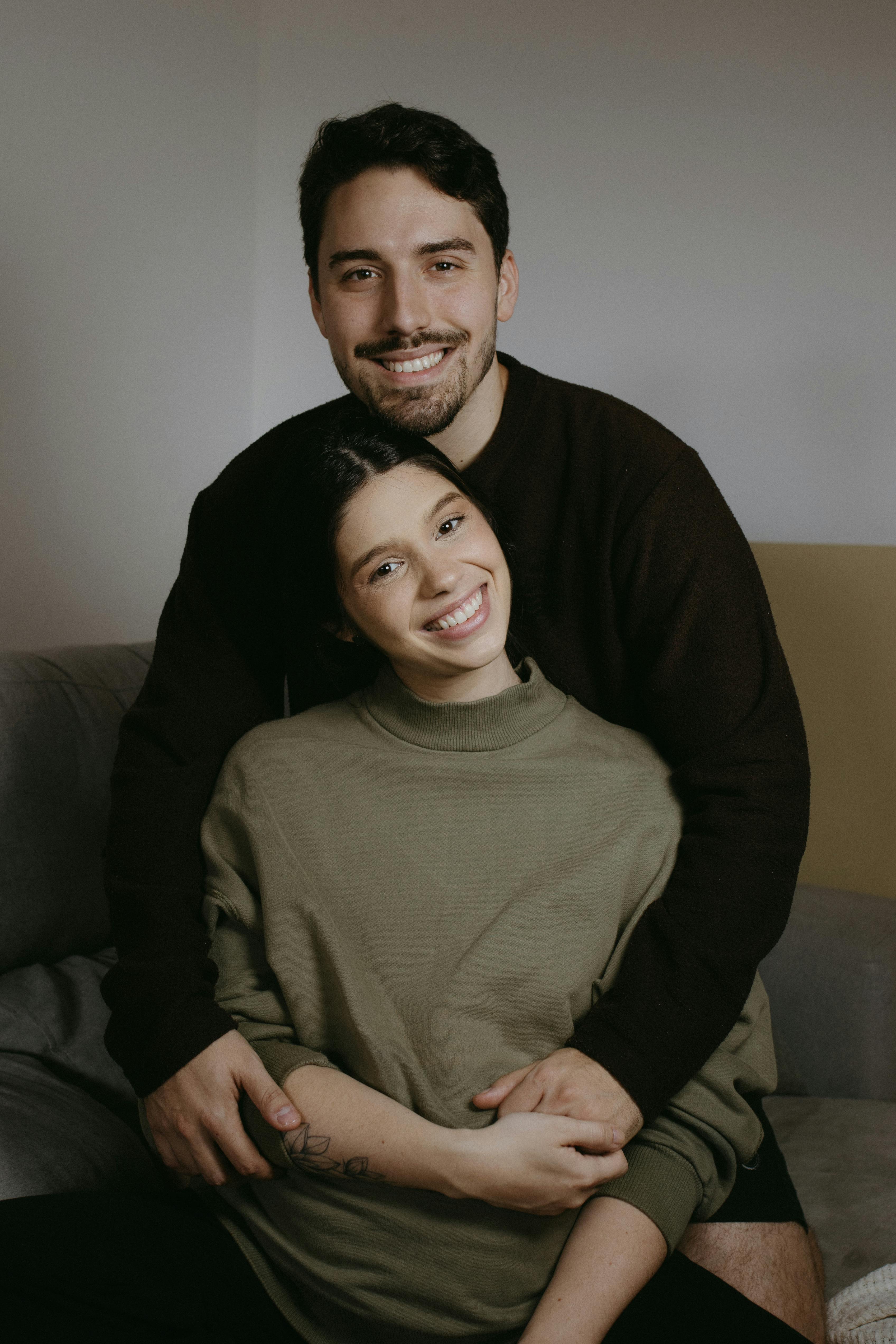 A man and a woman are smiling while sitting on a couch | Source: Pexels
