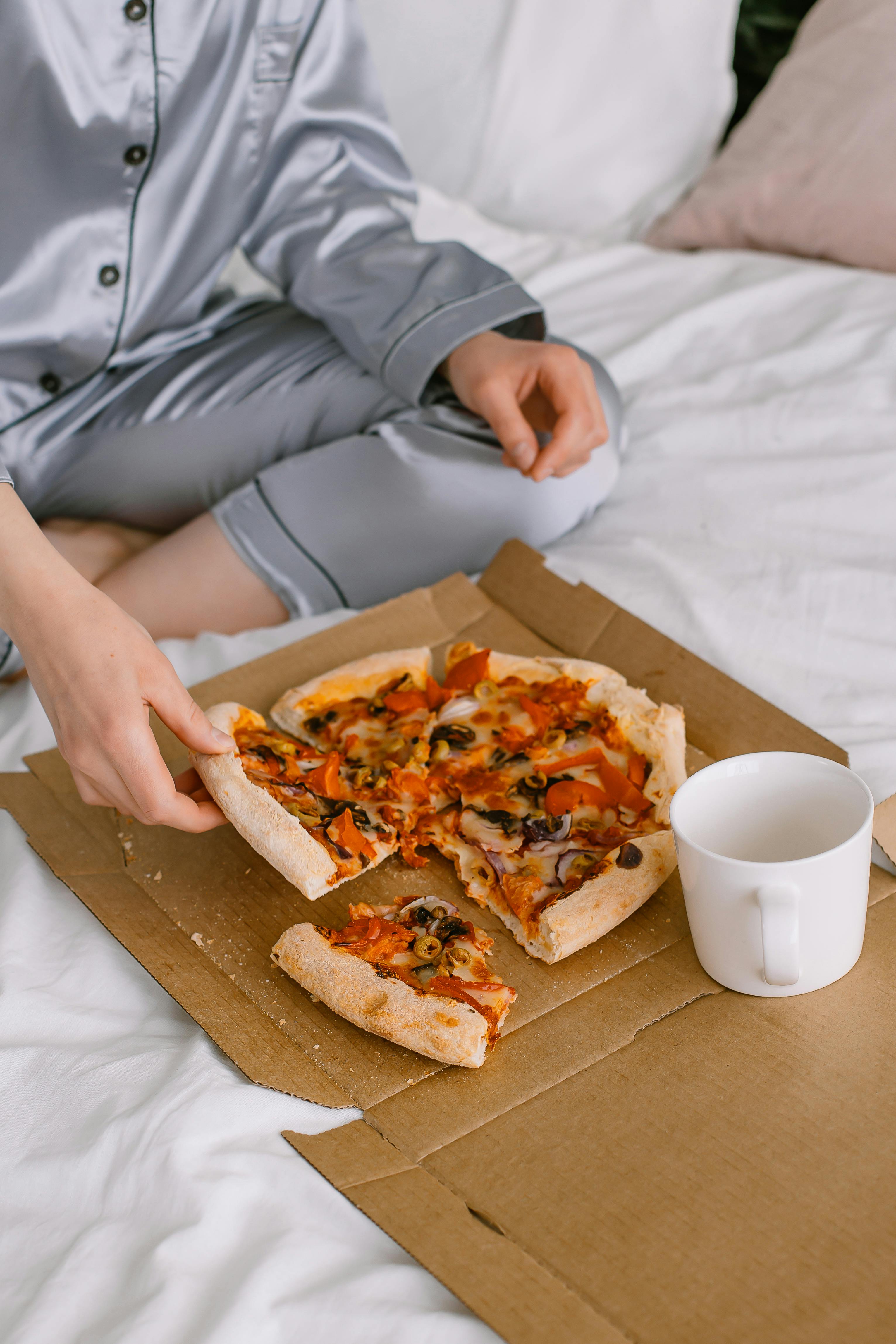 A person sitting on a bed with a box of pizza | Source: Pexels