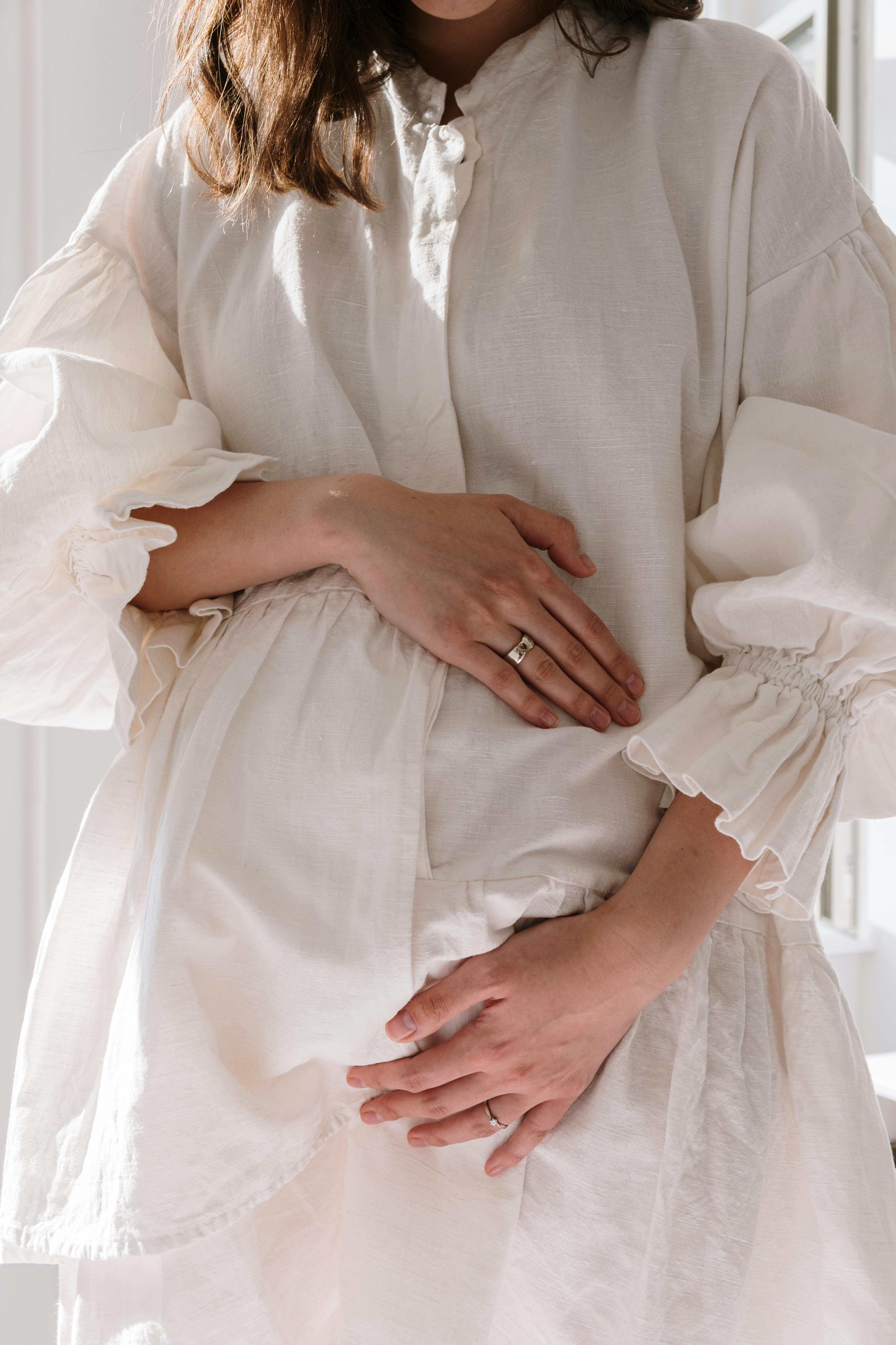 A woman in a white dress holding her belly | Source: Pexels