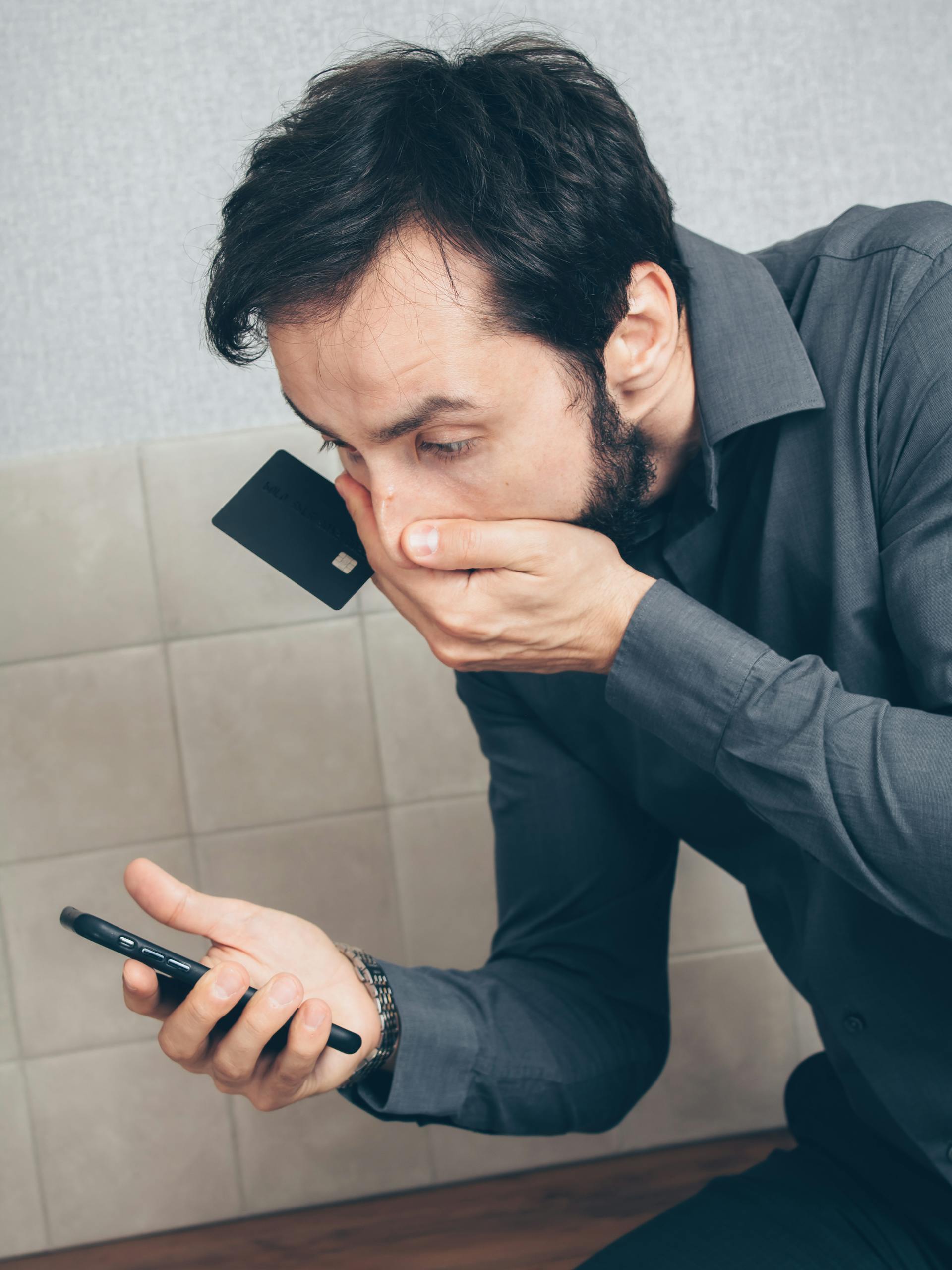 A man holding a credit card staring at his phone in shock | Source: Pexels