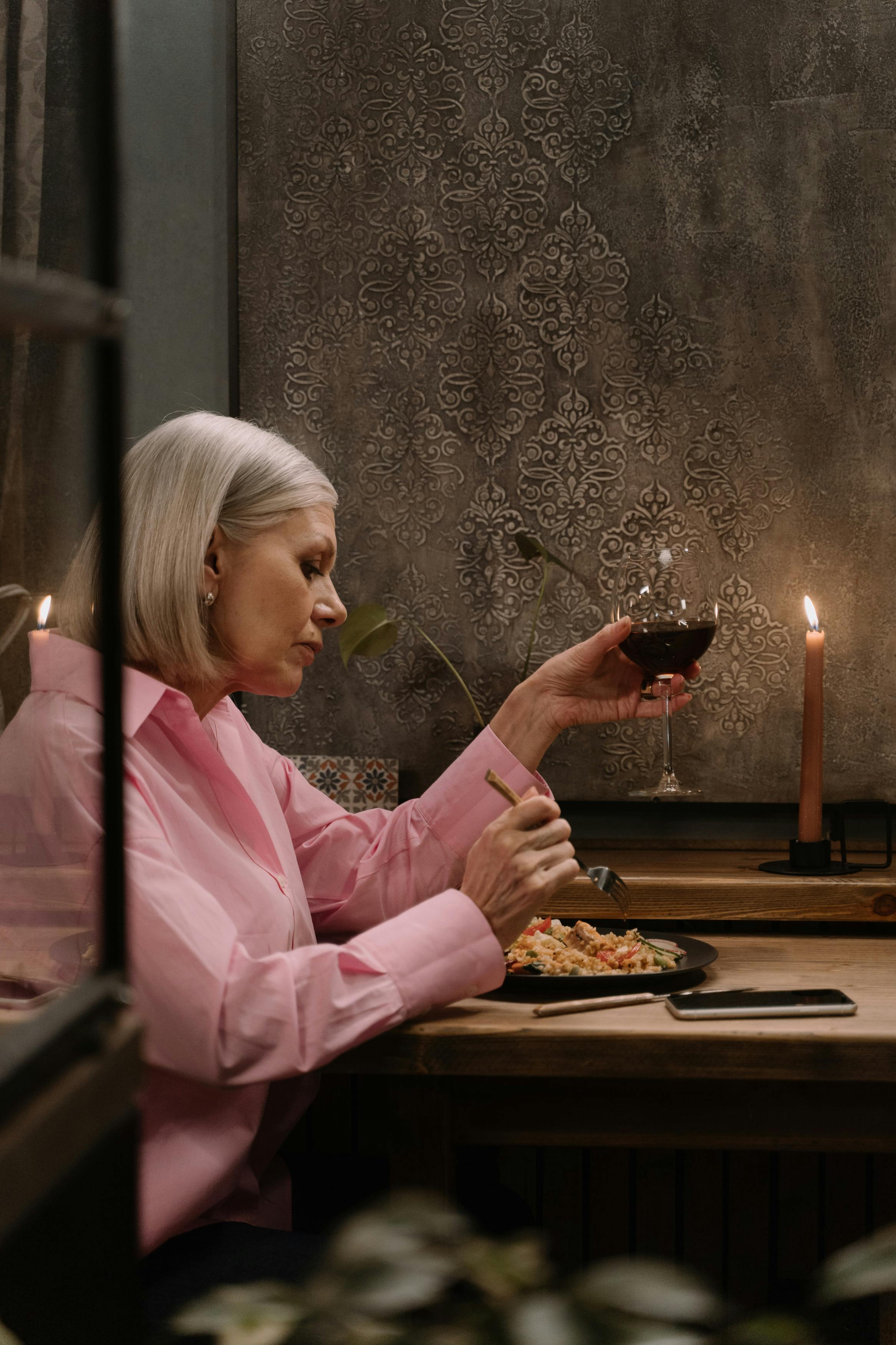 Woman holding a glass of wine while eating | Source: Pexels