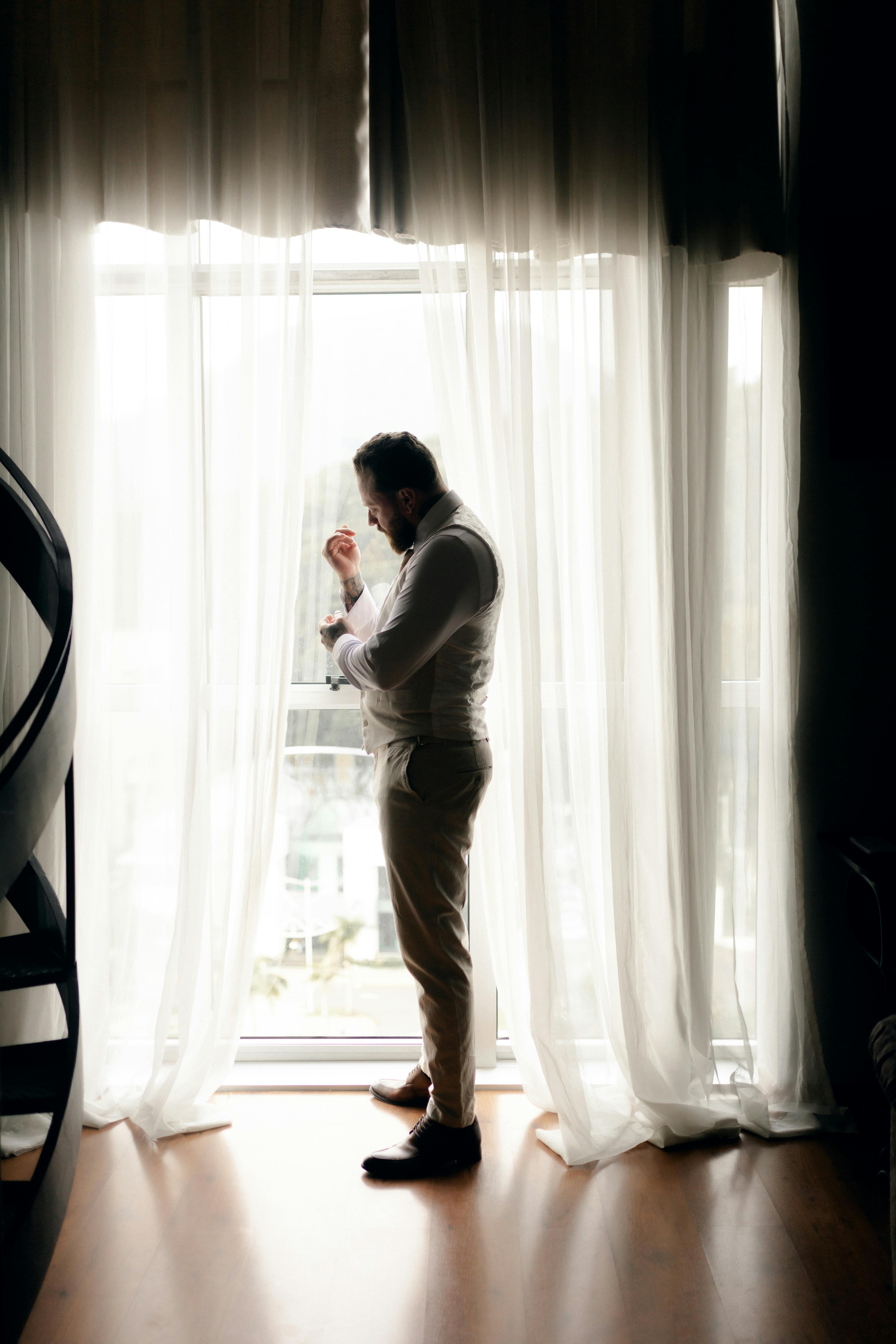 Man standing by the window adjusting suit | Source: Pexels
